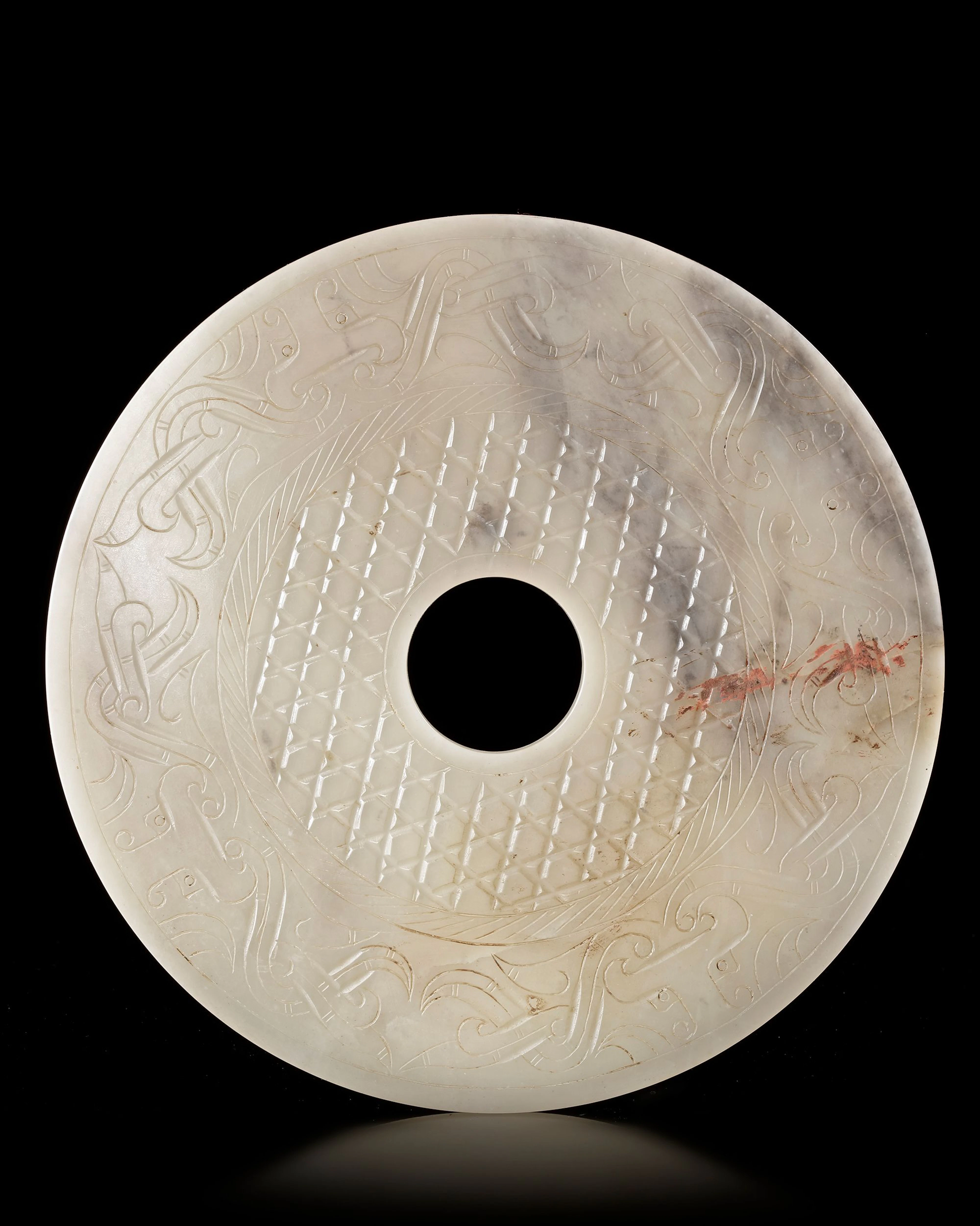 A CHINESE BI DISC DECORATED WITH A BORDER OF FOUR ANIMAL HEADS INTERTWINED