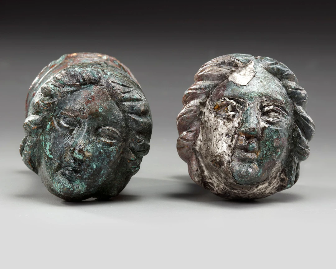 A PAIR OF ROMAN BRONZE AND SILVERED "FACE OF FEMALE" TERMINALS, CIRCA