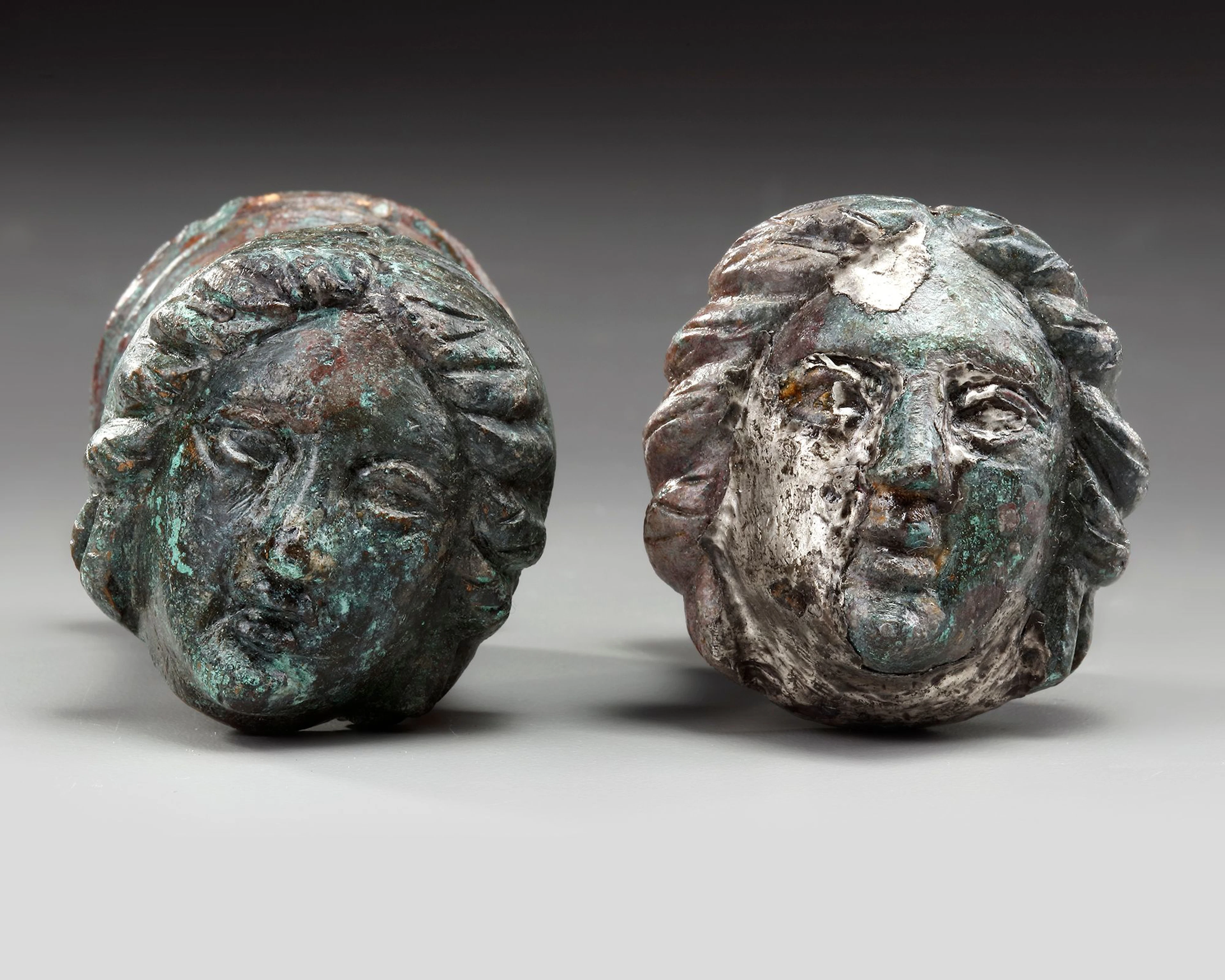 A PAIR OF ROMAN BRONZE AND SILVERED "FACE OF FEMALE" TERMINALS, CIRCA