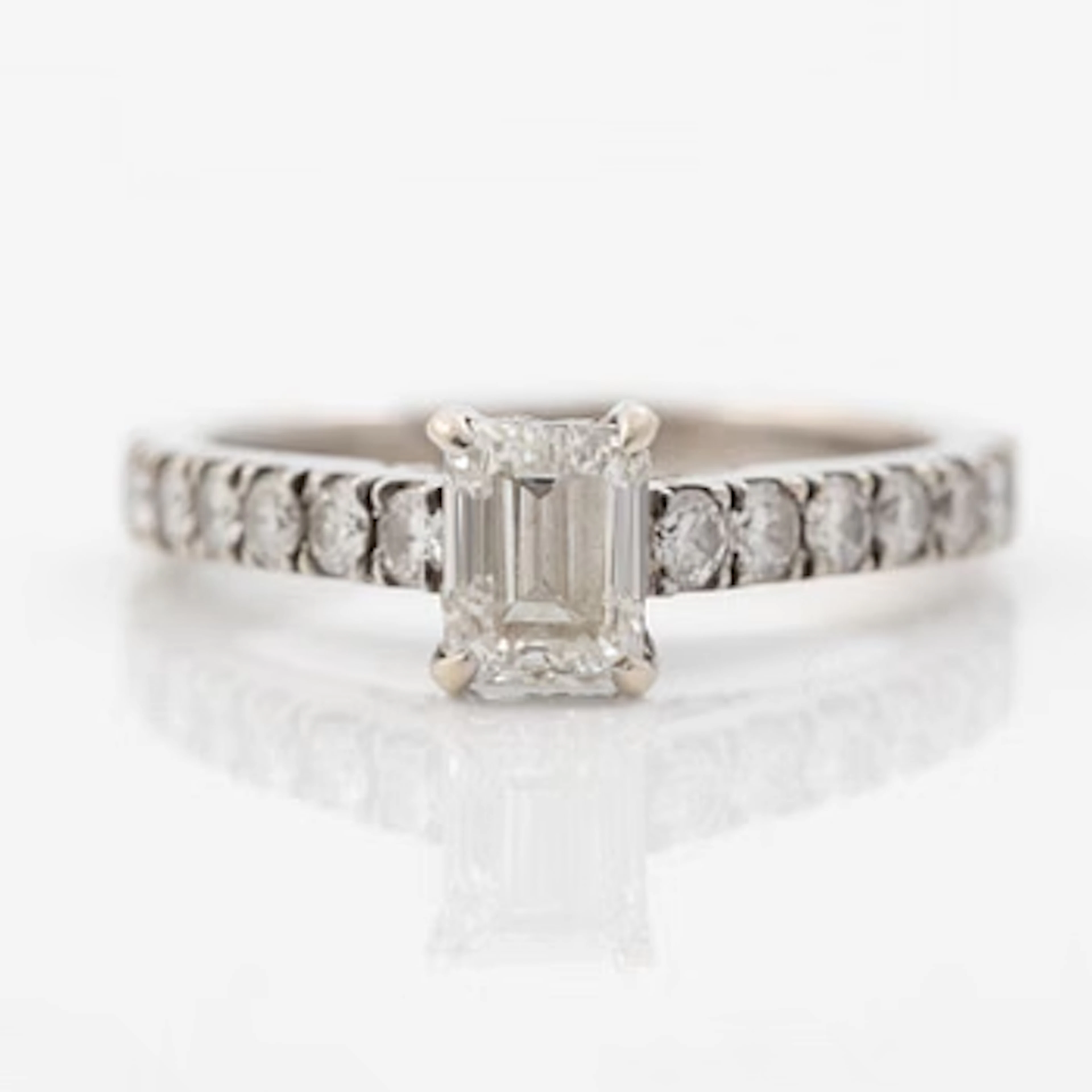 18K white gold ring set with an emerald-cut diamond and round brilliant-cut