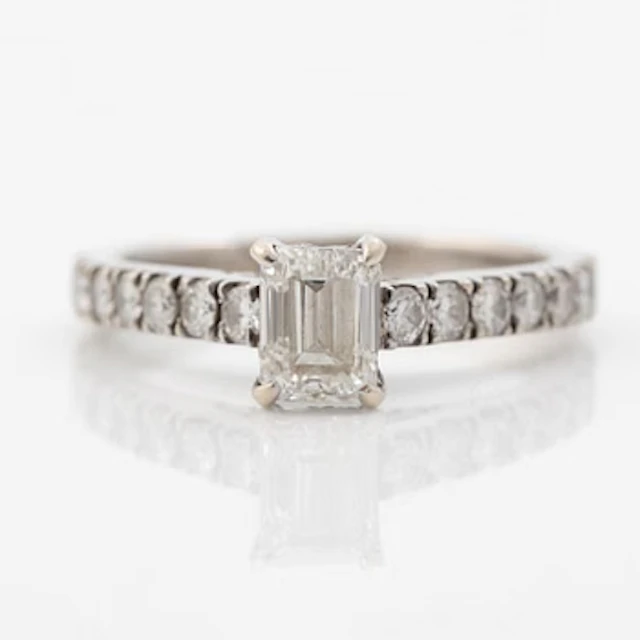 18K white gold ring set with an emerald-cut diamond and round brilliant-cut