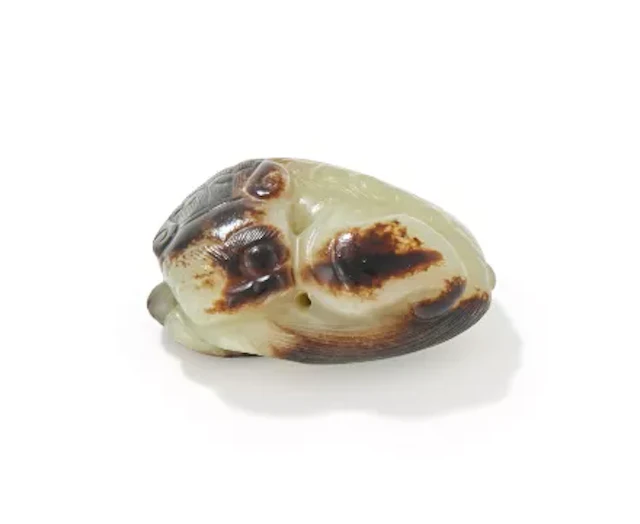 A Chinese celadon jade pendant of a recumbent Buddhistic lion, Ming Dynasty