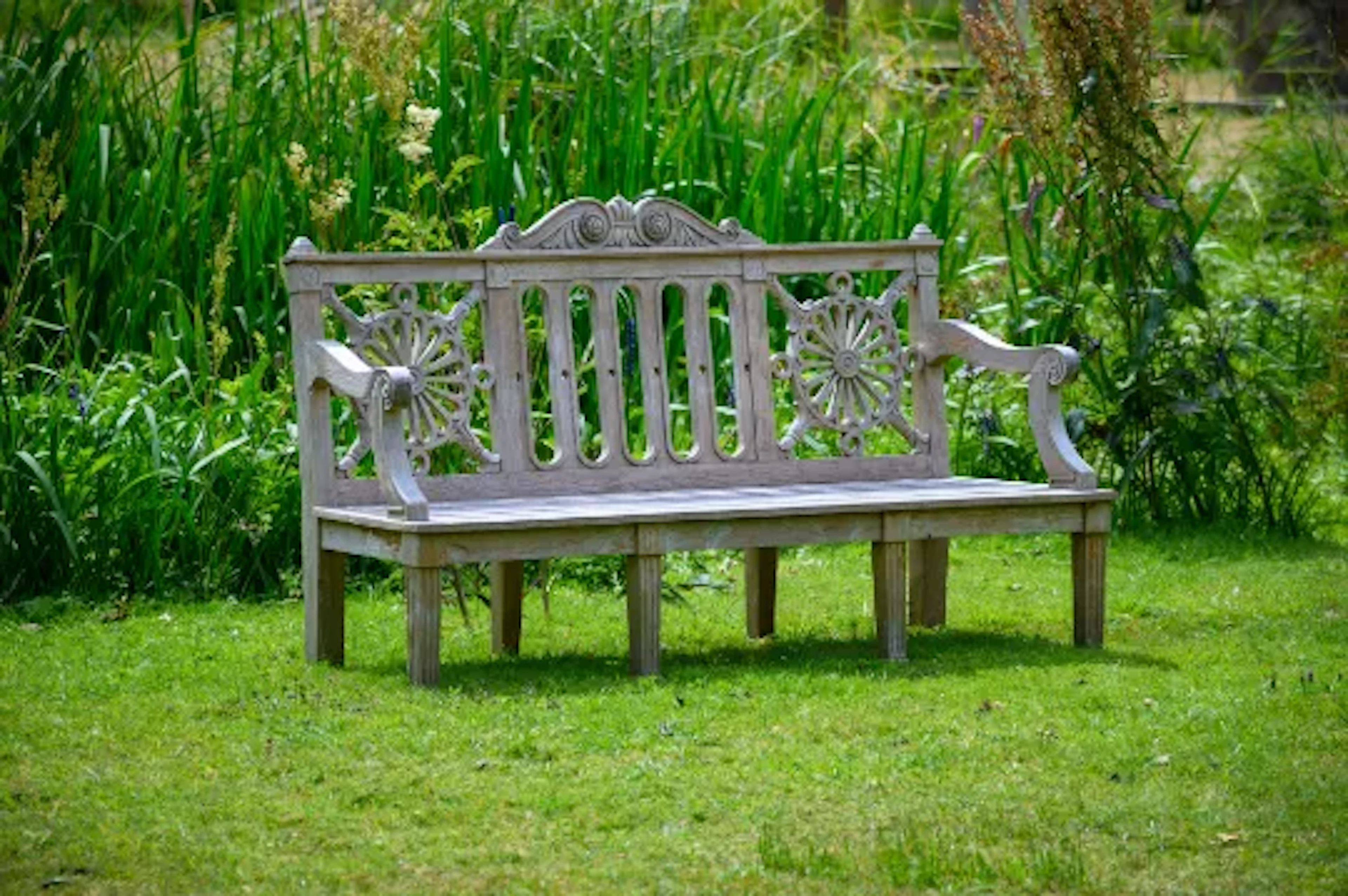 A CARVED TEAK 'HAREWOOD' GARDEN BENCH, IN THE MANNER OF THOMAS CHIPPENDALE