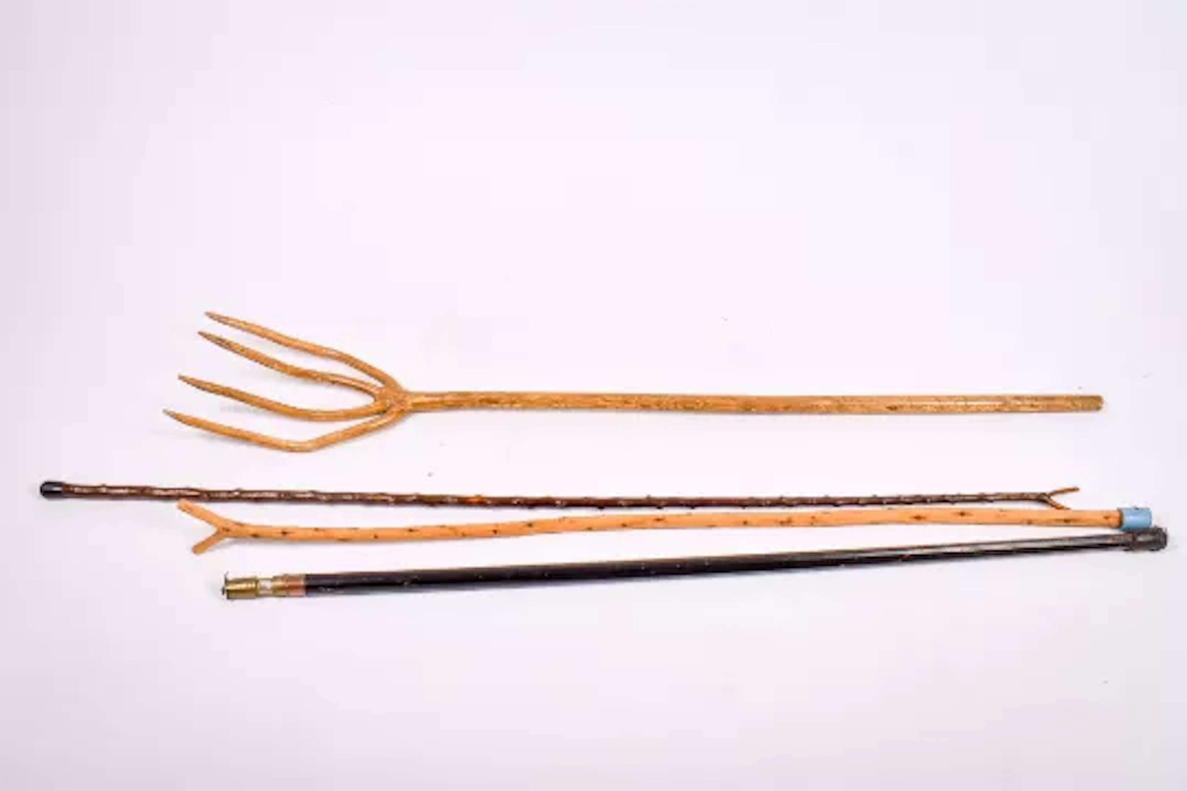 A group of three walking sticks and a natural wooden hay fork.