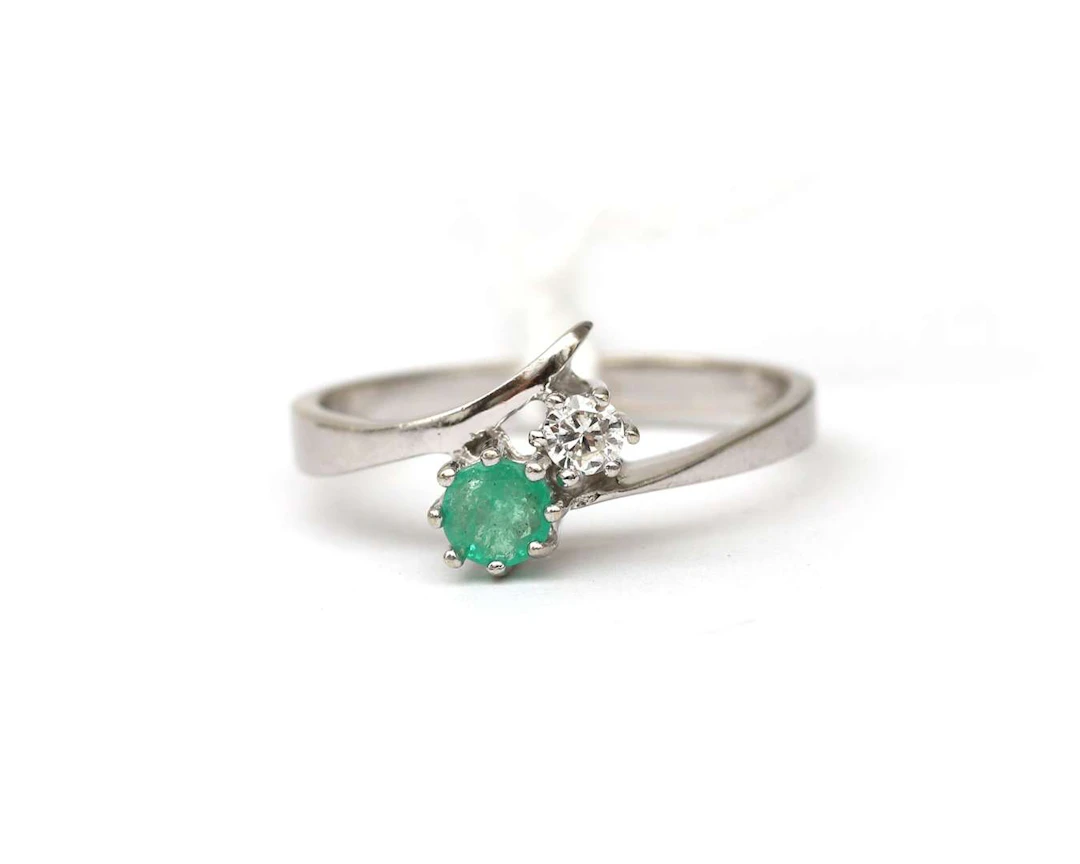 A 14k white gold bypass ring set with an emerald and a diamond