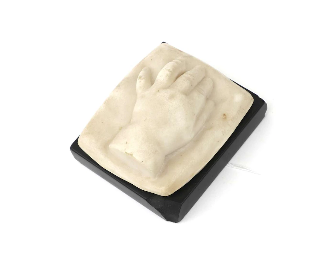 A small stone statue. A child’s hand. On a black stone plinth