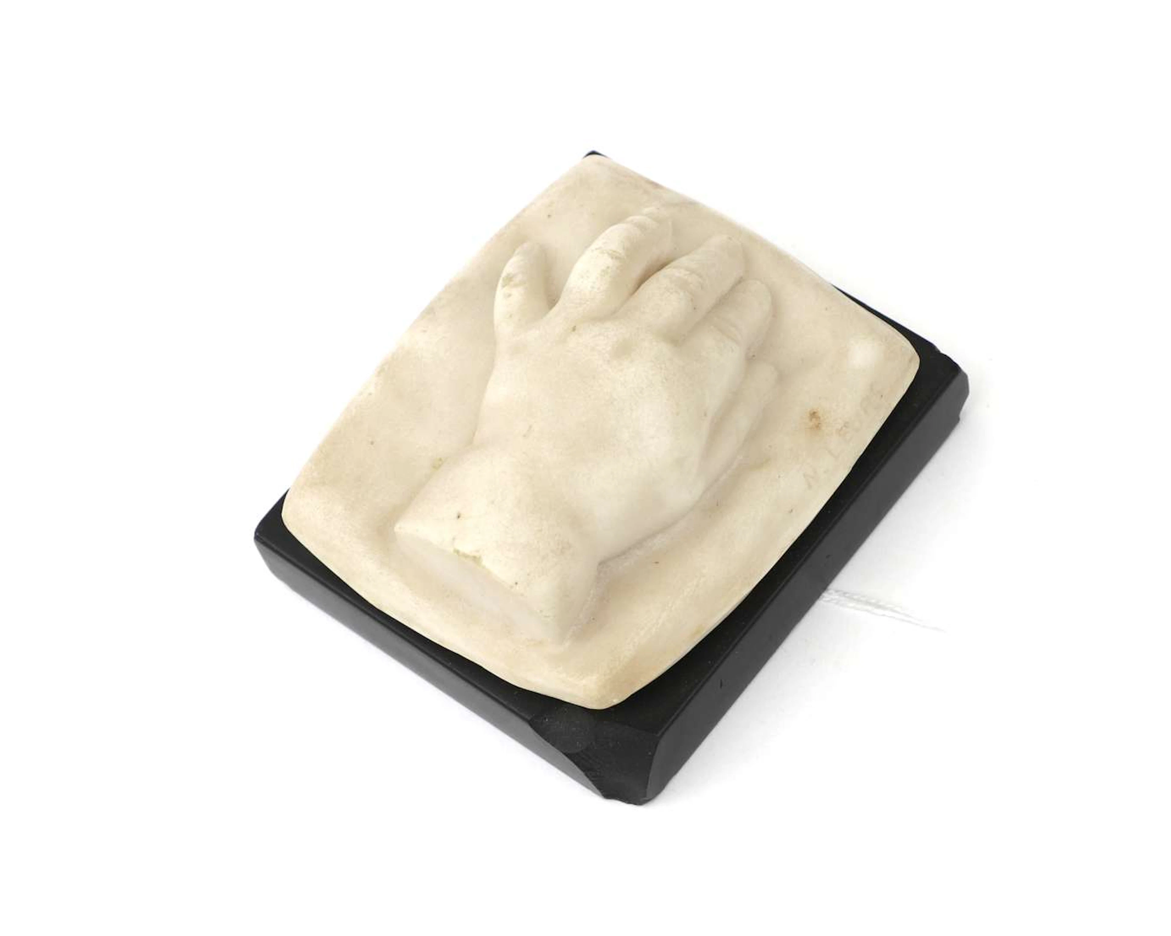 A small stone statue. A child’s hand. On a black stone plinth
