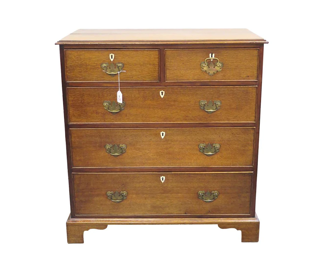 An oak chest of drawers with leg-mounted lock plates and brass fittings.