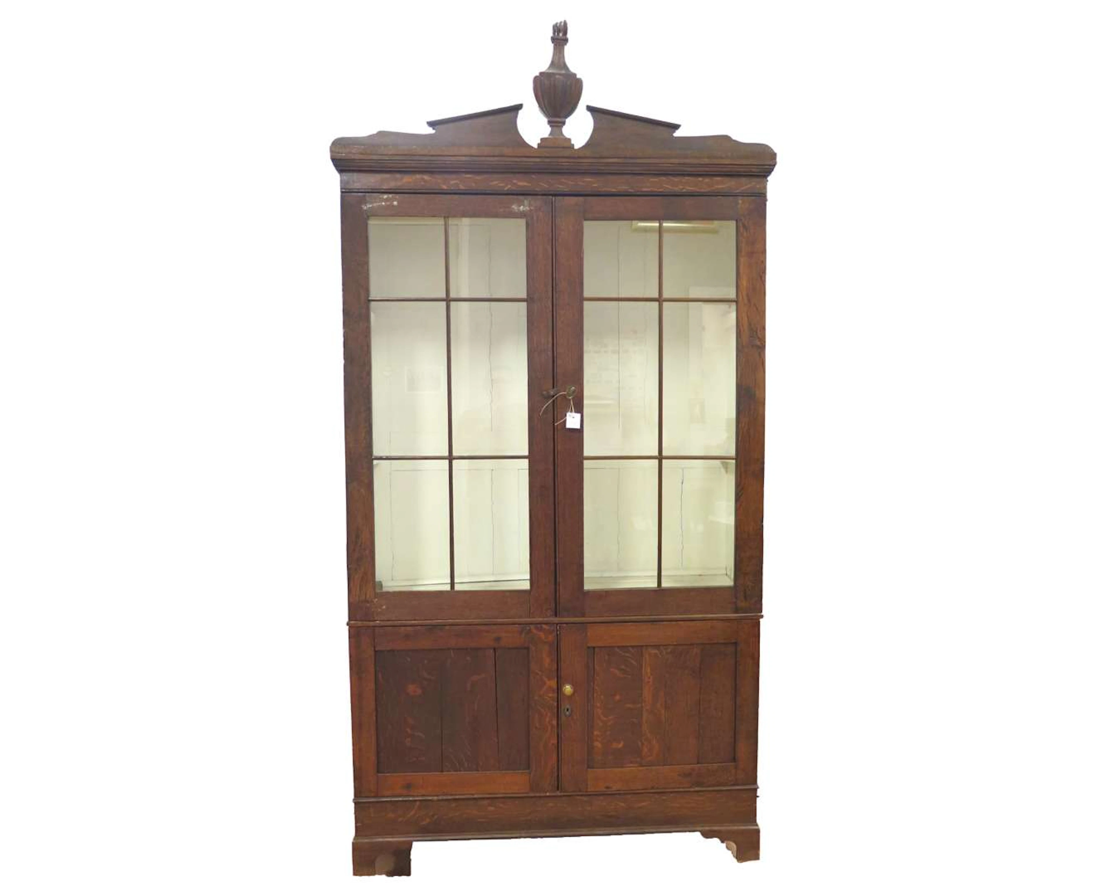 An oak display cabinet. The top features a vase ornament. 19th century