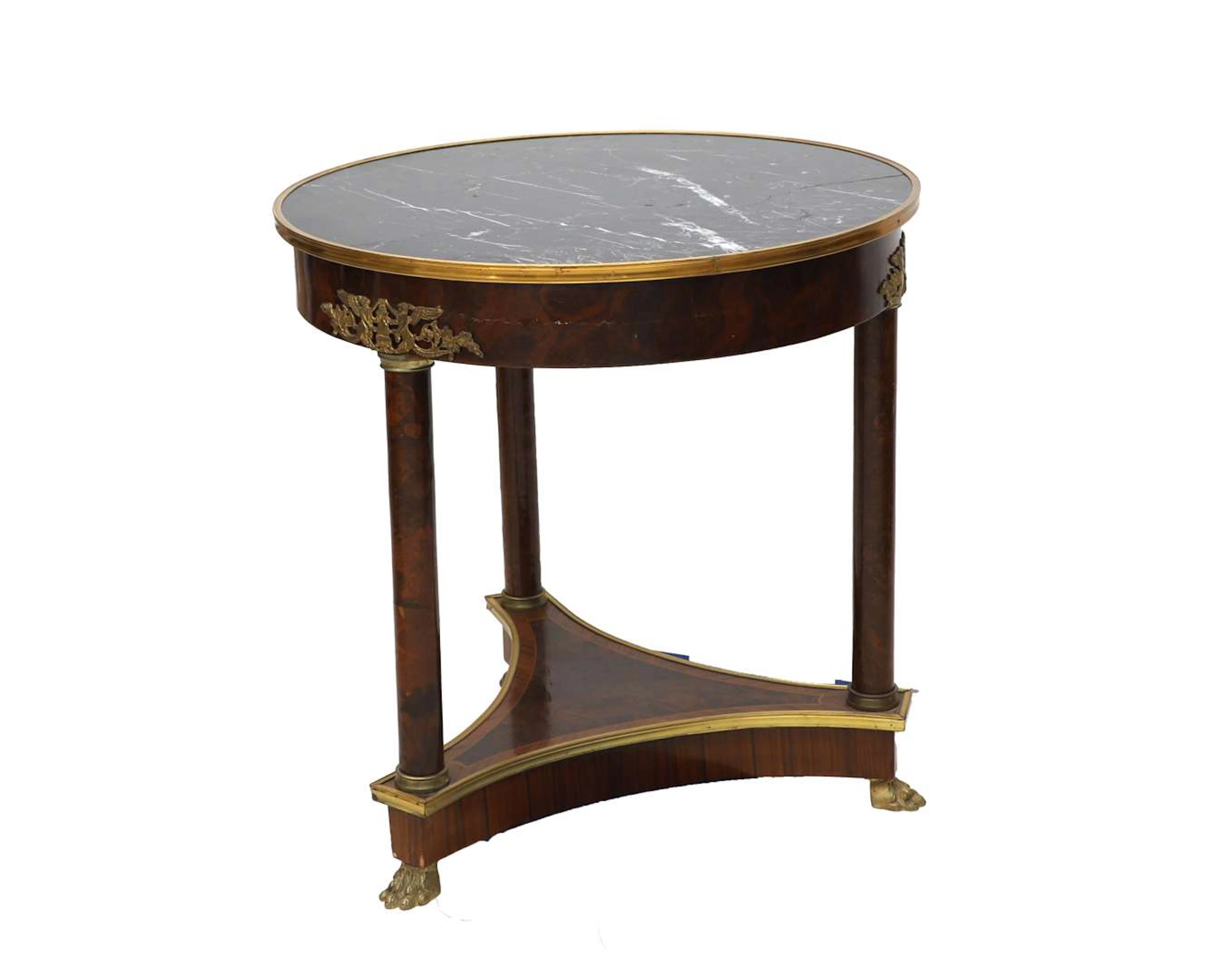 A round walnut table on three metal claw feet with a black marble