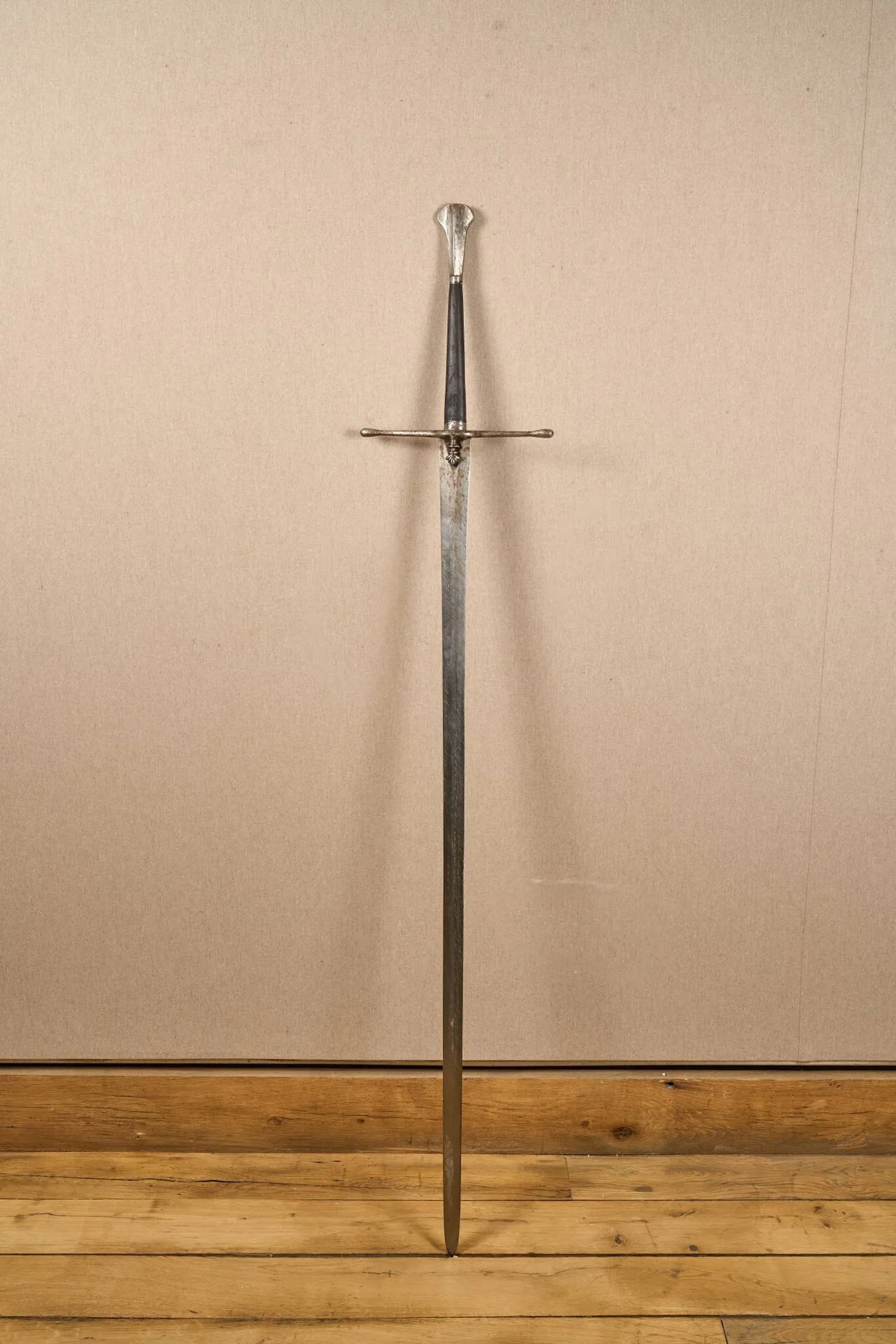 Forte épée à deux mains. Probablement d’inspiration écossaise pour la garde. Monture en fer. Pommeau à arrête médiane et fusée en bois noirci. Pièce de garde à deux quillons droits et croisière sculptée. Lame droite à arrête médiane. Longueur totale : 163 cm. Travail de style XVe siècle, probablement Violet le Duc.