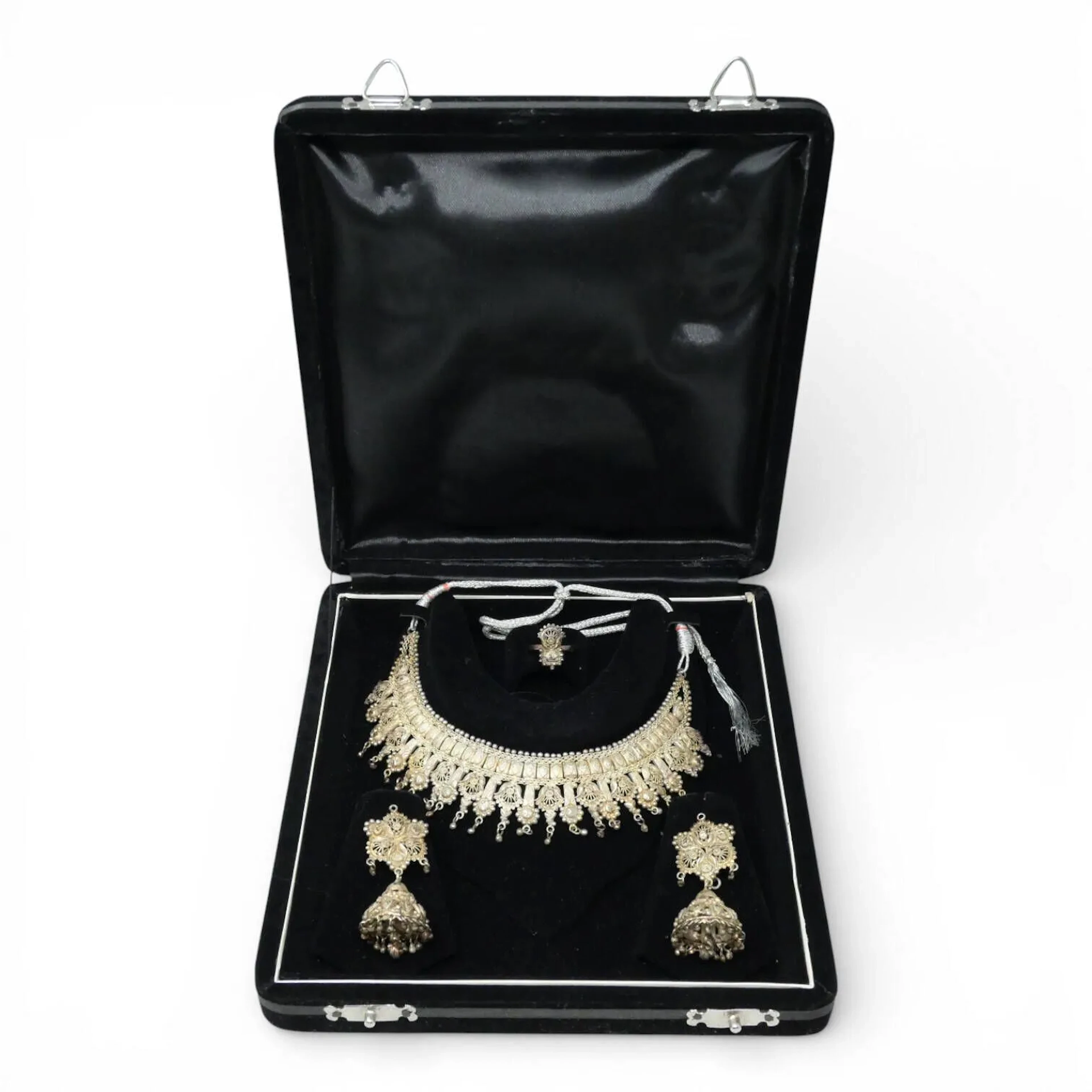 Suite de d'une parure et demi-parure en argent (800) comprenant : - collier et sa paire de pendants d'oreilles assorties, en argent ciselé réhaussés d'émail bleu et marron (accidents). Conservés dans un écrin - collier, paire de pendants d'oreilles et bague assortis, le tout formé de palmettes filigranées soulignées de grenetis, les pendants d'oreilles simulant des clochettes. Conservés dans un écrin. Tour de cou : réglable par cordon - tour de doigt : 60 Poids brut total : 95.71 g