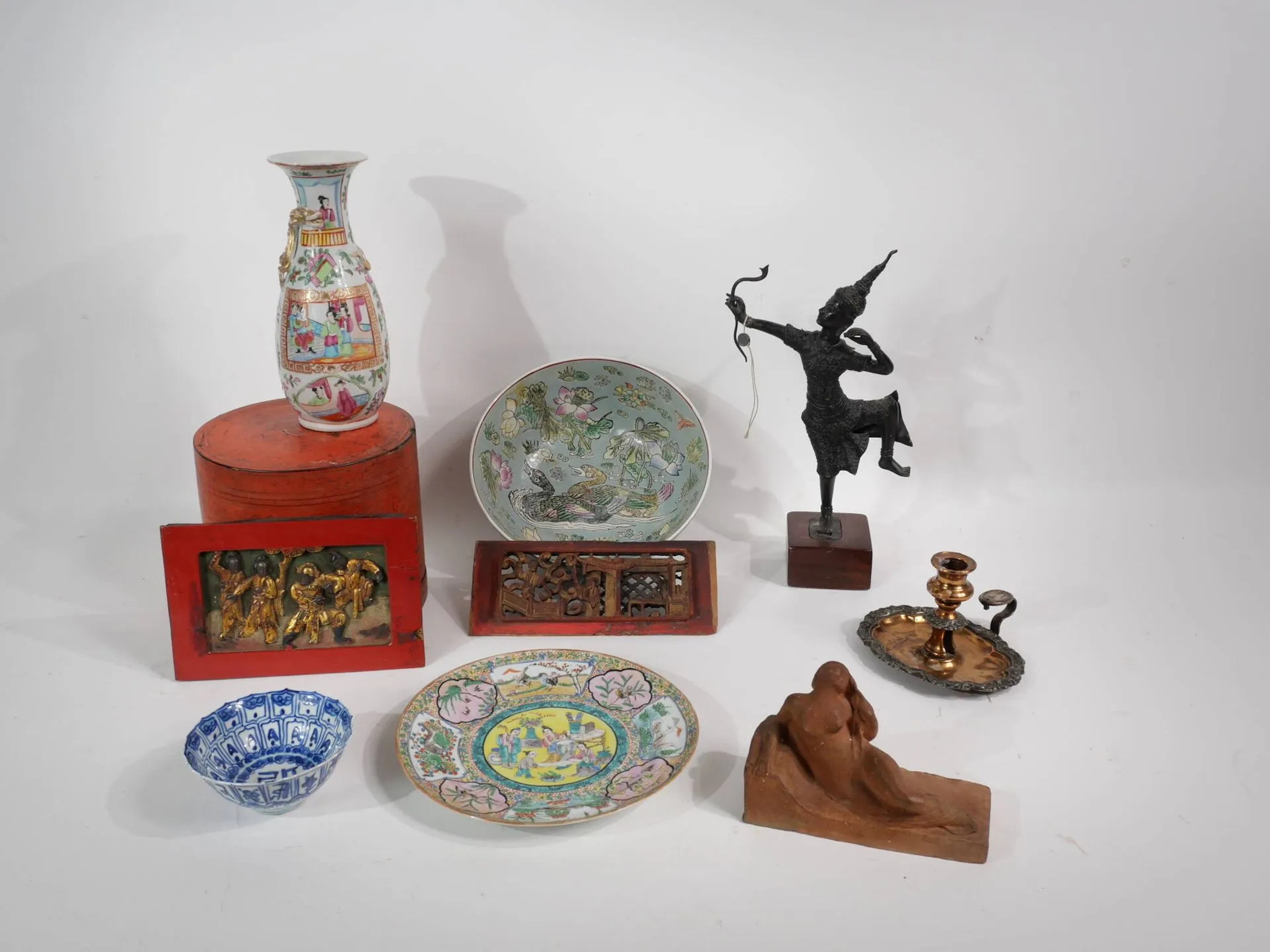 Lot de souvenirs majoritairement asiatiques comprenant : 2 petits panneaux sculptés patinés rouge et doré. 1 vase en procelaine Canton 1 statuette Thailande Archer 1 boite laquée à compartiment 1 assiette Chine fond jaune, scène animée 1 Coupe chine décor de canard, diam : 25,5 cm. 1 bol blanc bleu 1 bougeoir à main décor argenté 1 terre cuite, femme allongée non signée, longueur : 18 cm.