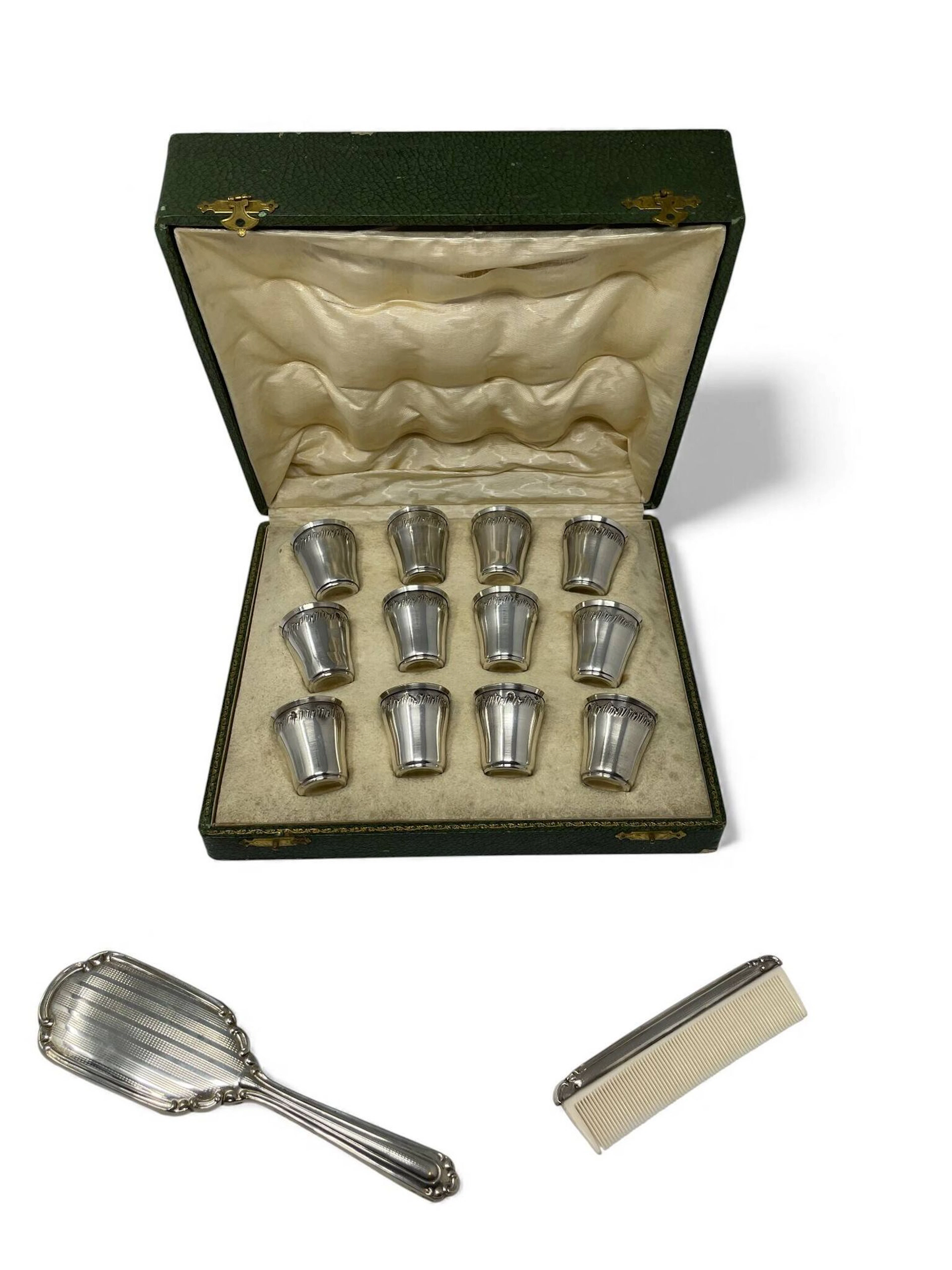 Suite de 12 verres à liqueur (950) en argent à décor au repoussé de feuillages. Intérieur vermeillé. Poids: 111,4 gt Chocs Dans un écrin On y joint un nécessaire de toilette comprenant un peigne et une brosse en argent (800) à décor de volutes et guillochages. Poids brut: 75,3 gr Dans leur boîte