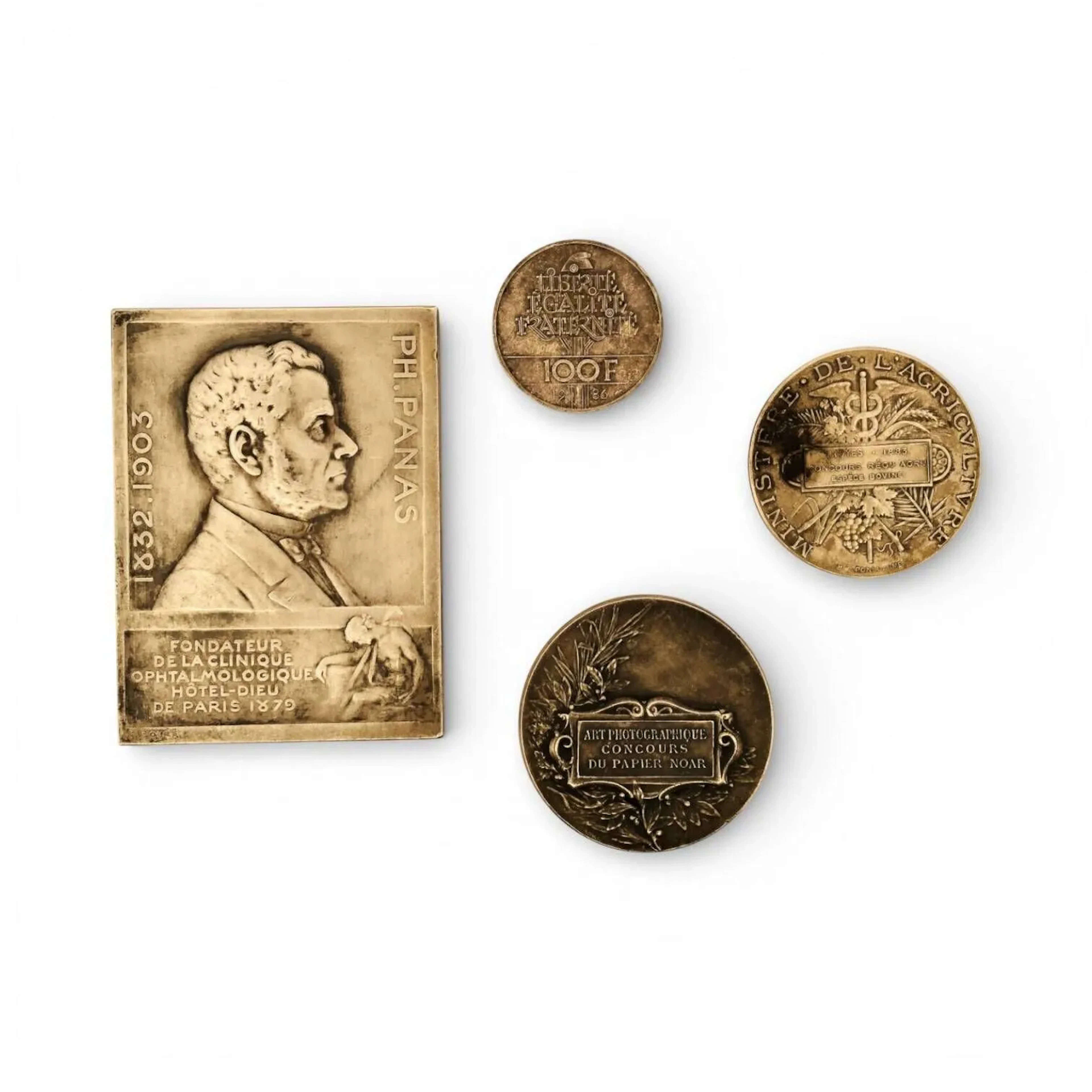 Ensemble de médailles et plaque comprenant: - Louis BOTTEE (1852-1940) : Arte et. Studio. Tenebris. In.Lucem.Evocat. Portrait de Ph. Panas. (1832-1903) – Fondateur de la Clinique Ophtalmologique Hôtel Dieu de Paris 1879. Plaque de table en argent (800 min.) Début XXème siècle Titre: corne d'abondance Dim. 7,7 x 5,7 cm. Poids: 129, 4 g - Médaille en argent (950) de forme circulaire Avers: Femme assise à son bureau tenant dans ses mains une photographie, une chambre photographique à sa gauche. Inscription "LA PHOTOGRAPHIE" Revers: Cartouche titré "ART PHOTOGRAPHIQUE CONCOURS DU PAPIER NOAR" et branche de laurier en fond Marque sur la tranche M/M, ARGENT, 950 Titre: Tête de sanglier, Orfèvre illisible Poids: 46,8 gr - H. PONSCARME, d'après Médaille en argent (800 min.) de forme circulaire Avers: : inscriptions "Ministère * de * l'Agriculture" "Troyes * 1885 * Concours Régle Agrle Espèce Bovine" sur fond de caducée, pampres de vigne et épis de blé Revers : décor du portrait allégorique de la République Française. Titre: Corne d'abondance Poids: 38,4 g - Pièce commémorative - Centenaire de la statue de la Liberté (1886-1986). 100 francs Statue de la Liberté en argent (925) Avers: La statue de la Liberté est survolée de onze oiseaux. Elle est accompagnée des dates "1886-1986" et de l'inscription : "RÉPUBLIQUE FRANÇAISE" Revers : Un arbre surmonté d'un bonnet phrygien a pour feuillage la devise : "LIBERTÉ ÉGALITÉ FRATERNITÉ". Marque d'atelier de Monnaie de Paris - Différent Dauphin: Émile Rousseau, Graveur général des monnaies, Monnaie de Paris (1974-1994) Poids: 15 gr