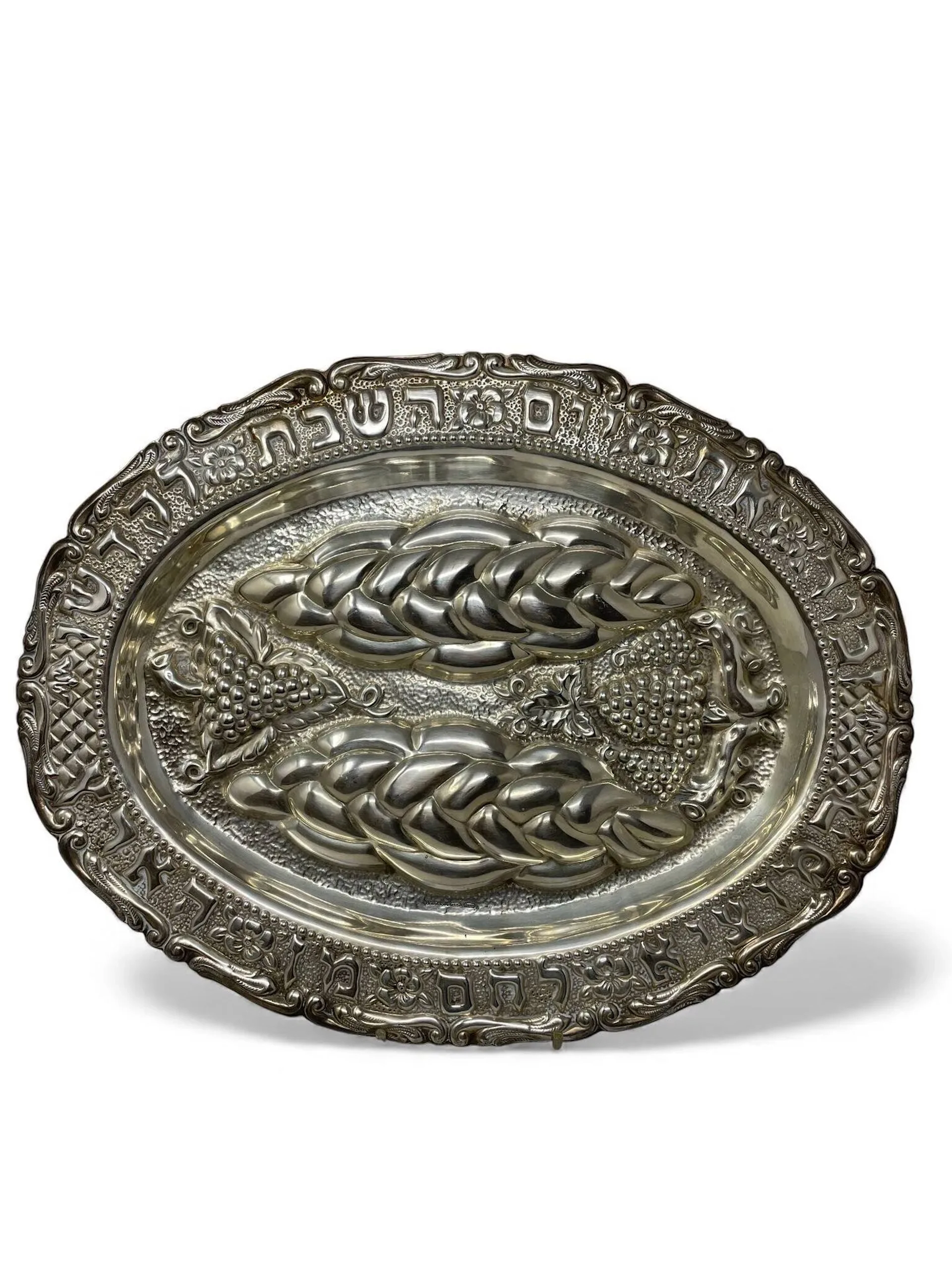Plat à Halla de forme ovale en argent (925) à décor au repoussé de pampres de vignes et halla sur fond martelé dans le bassin, l'aile mouvementée richement décorée au repoussé d'inscriptions hébraïques, fleurettes, feuillages et frise de perles. Florence (Italie), XXème siècle Poinçon de titre, poinçon de responsabilité, Orfèvre: Hazorfim Poids: 597,7 gr 79,5 x 30,5 cm