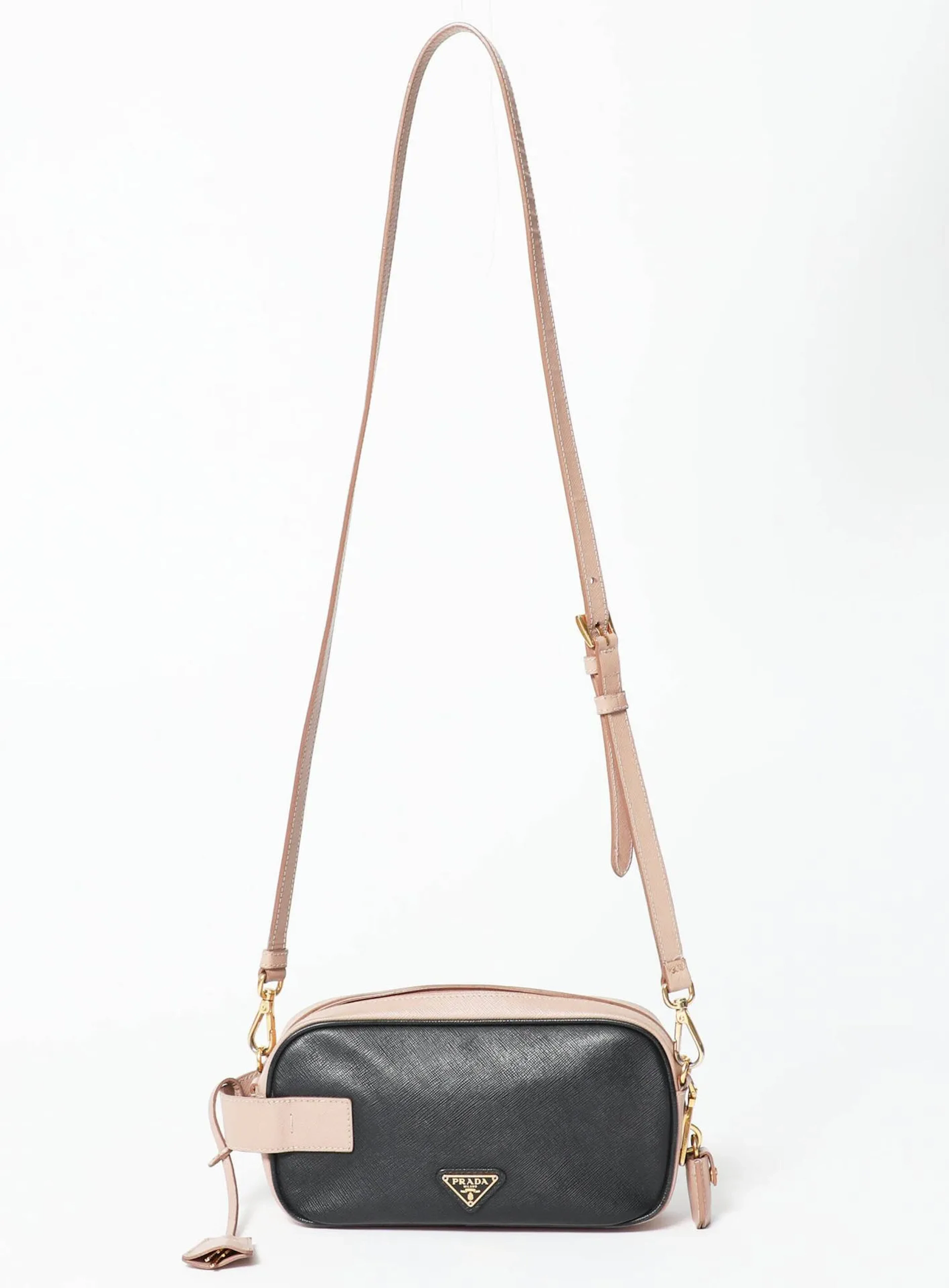 PRADA Sac bandoulière ou épaule façon camera en cuir Saffiano bicolore noir et rose poudré à intérieur agneau lisse, signature centrale à dominante dorée. Légères usures, frottement. Dimensions : - Longueur : 21cm - Hauteur : 11cm - Largeur : 8cm - Hauteur de chute : 20cm