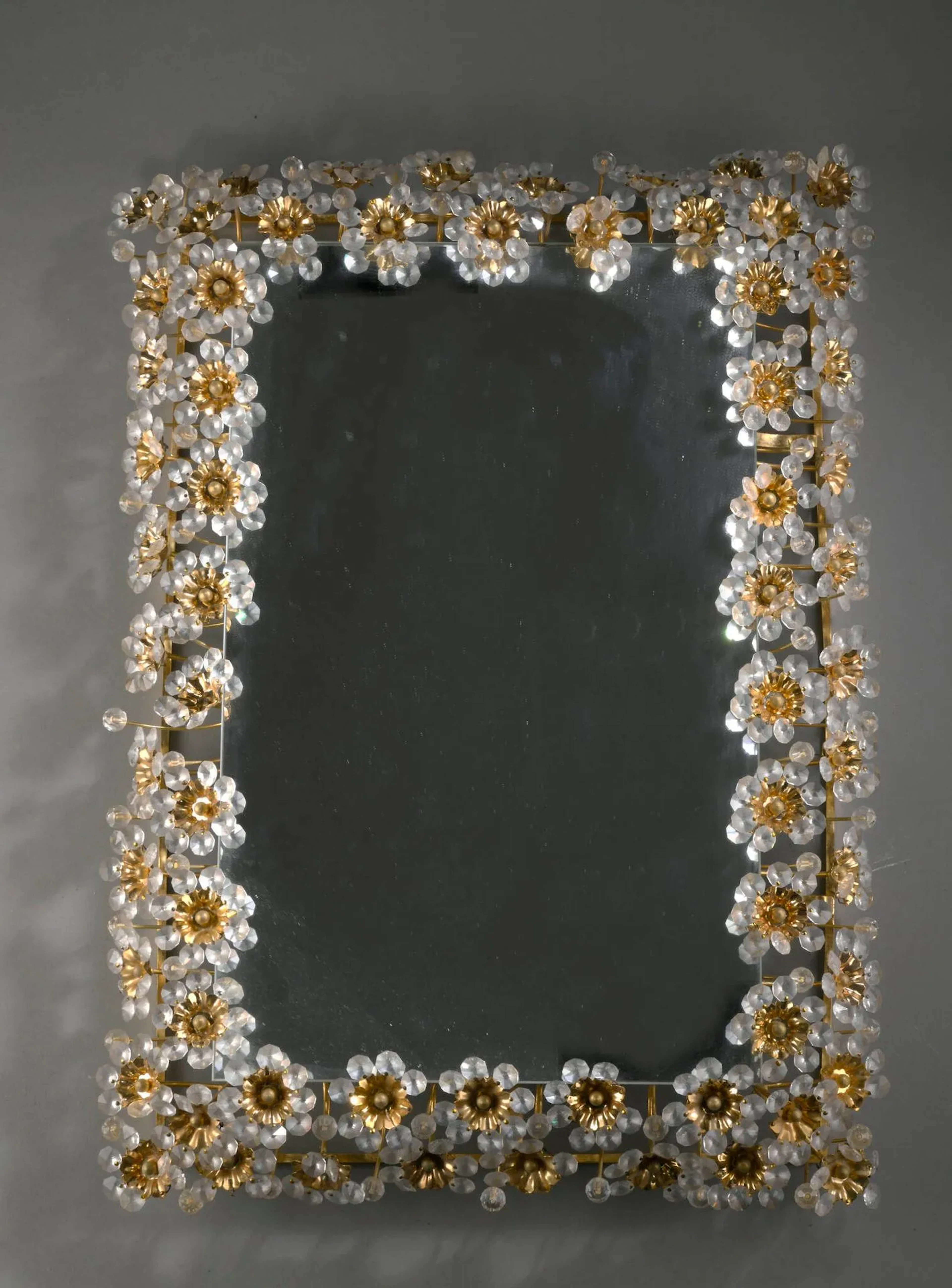 TRAVAIL ALLEMAND (XX) Miroir mural rectangulaire lumineux, circa 1970, à encadrement en laiton à décor de fleurs à pistil en métal doré et de pétales en cristal (Manques, rayures, usures, système électrique à revoir) H.: 58 cm. - L.: 44 cm.