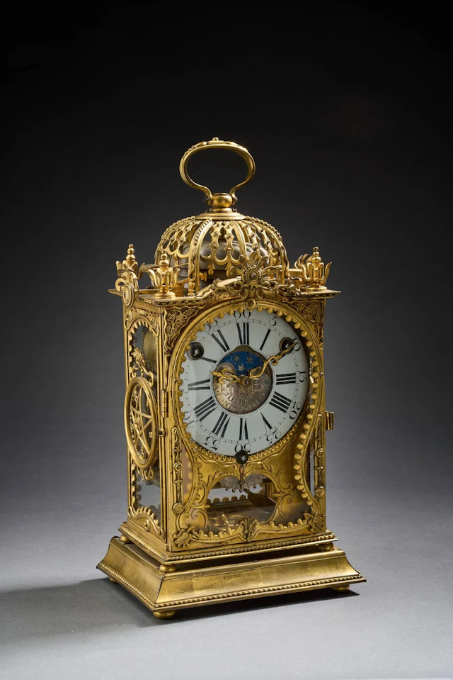 Pendule d’officier montée à cage en bronze ciselé et doré. La base à doucine bordée d’un cordon torsadé. Riche décor ajouré de motifs mouvementés, réserves, lambrequins, feuillages en applique. Les côtés ornés d’un pentacle ajouré. Le sommet en dôme, dissimulant trois timbres, est flanqué de turlupets. Cadran annulaire à chiffre arabes et romains, signé « LEFEBVRE à Fontainebleau ». Dateur en partie basse. Mouvement à complication. Probablement Jean Lefebvre, maître en 1733, il devient horloger du roi. Il est actif à Fontainebleau et à Paris. Travail de la seconde moitié du XVIIIème. 32 x 18 x 12,5 cm (Fonctionnalité du mouvement non garantie, restauration au mouvement). Le Metropolitan Museum de New York, conserve sous le numéro d’inventaire 29.52.17, une pendule de ce même maître. Une pendule similaire était présentée chez Fraysse le 4 juin 2008, lot 221. Bibliographie : Dictionnaire des horlogers français, Tardy, 1972.
