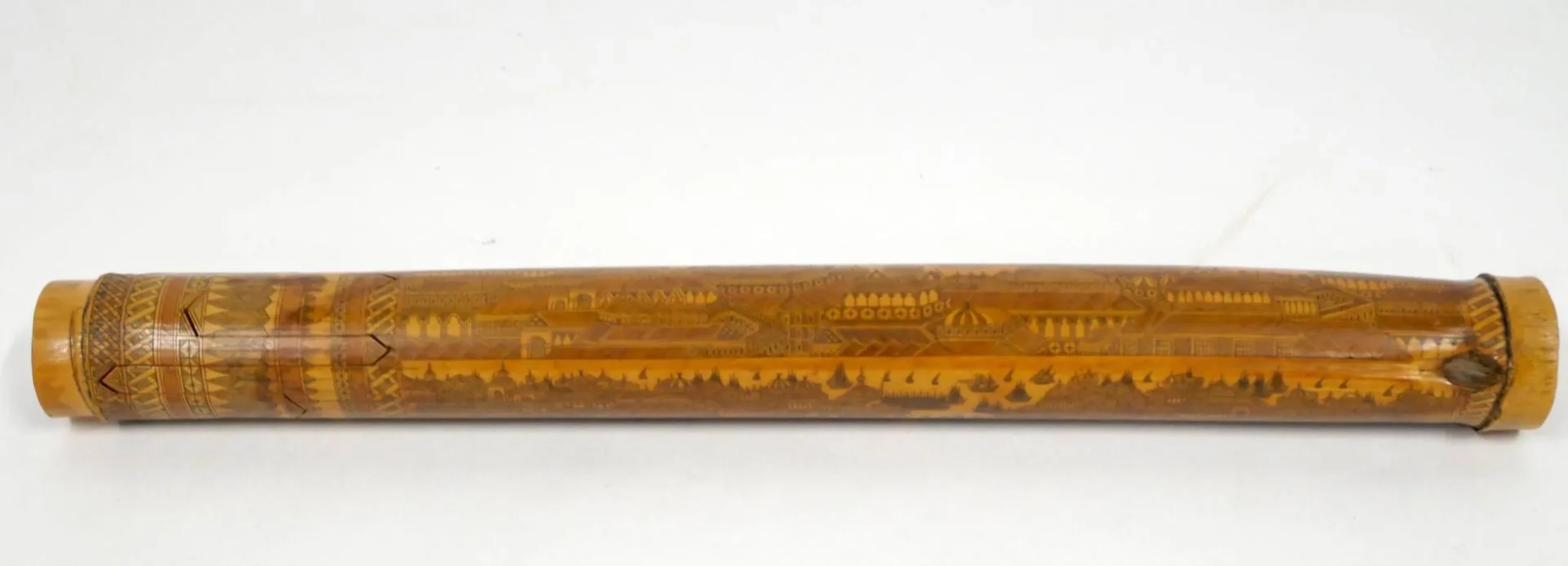 Travail artisanal algérien, fin du XIXe siècle Étui à courrier cylindrique en bambou gravé à décor panoramique continu représentant un grand port oriental, probablement une vue stylisée de Constantinople. Sans inscription ni date. Longueur : 26,7 cm. La surface du bambou est entièrement décorée par incision fine figurant une ville portuaire animée de nombreux navires marchands et embarcations, devant un ensemble architectural dense composé de mosquées à coupoles surmontées de croissants, pavillons, terrasses et constructions fortifiées disposées le long du rivage. La composition se développe en frise continue sur toute la longueur de l’objet. L’iconographie demeure volontairement stylisée et synthétique, caractéristique des productions orientalistes de la seconde moitié du XIXe siècle, dans lesquelles les grandes villes du Levant – notamment Constantinople – sont évoquées par une accumulation de coupoles, minarets et bâtiments monumentaux plutôt que par une représentation topographique précise. La technique de décor repose sur une gravure par incision directe dans la surface du bambou, les traits étant ensuite accentués par un noircissement des sillons afin de renforcer le contraste avec la matière claire. Des procédés comparables sont observés sur certains objets en bambou gravé produits en Algérie au XIXe siècle, notamment sur des instruments de musique traditionnels de type nay. Ces objets relèvent d’une production artisanale développée en Algérie durant la période coloniale, destinée en grande partie aux voyageurs, visiteurs étrangers et militaires en séjour. Ils étaient souvent réalisés comme objets-souvenirs ou pièces décoratives mettant en scène des vues orientalistes très appréciées dans l’Europe du XIXe siècle. Œuvres en rapport : – Flûte à embouchure terminale de type nay en bambou gravé, travail algérien, musée de la Philharmonie de Paris, inv. E.2002.8.3. – Étui en bambou gravé représentant une vue du port d’Alger, portant l’inscription gravée « Hamourba Ben ElhaJ, Rue des Pyramides n°15, Alger, Médaille 1876 Exposition d’Agriculture », vente Archéologie, Arts d’Orient, Boisgirard – Antonini, Paris, 28 novembre 2013.