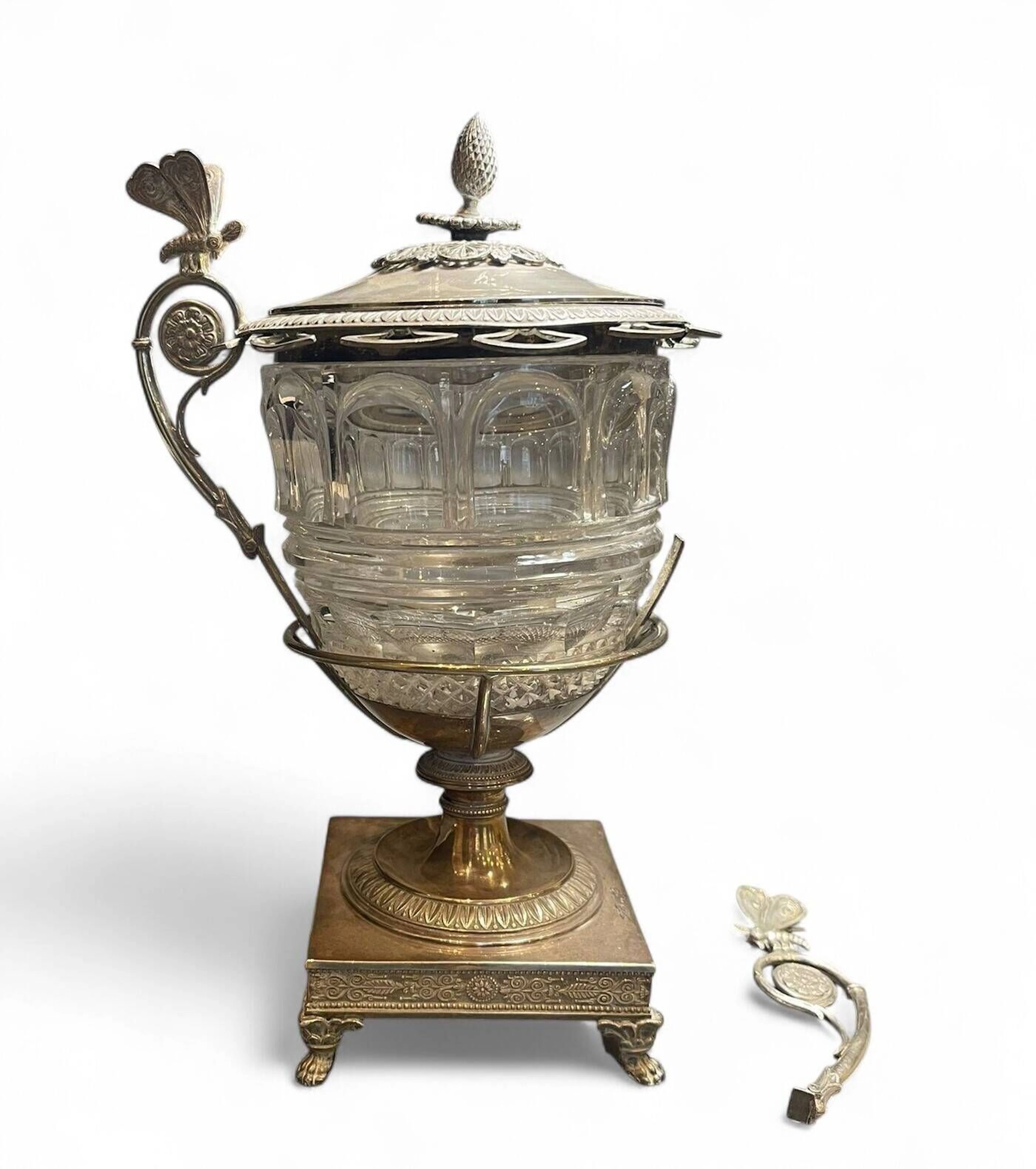 Confiturier en argent (950) (Michel-Ange) (Cérès de grosse garantie parisienne) à décor de palmettes, pieds griffes et anses ornées de papillons. Paris, époque Restauration (1819-1838). Une anse cassée, structure cabossée. Manque les cuillères. Poids brut : 1034,00g.