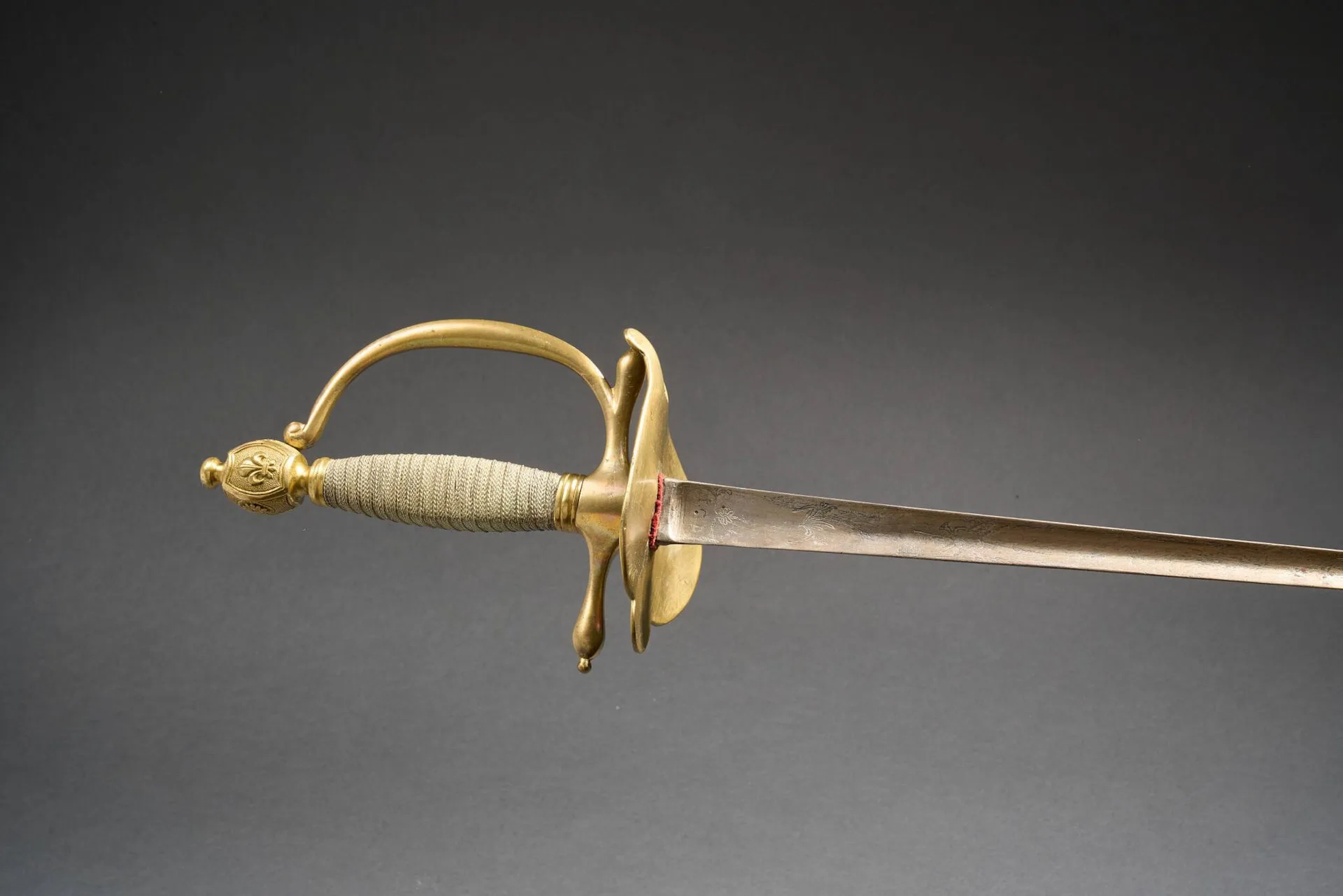 Épée des chevaux légers de la maison militaire du roi modèle 1814. Monture en bronze doré. Pommeau en forme d’olive au profil du Roi Henri IV. Garde à une branche et deux quillons droits marquée « 1593 » au nœud de corps. Clavier aux armes de France sous couronne royale flanquées de drapeaux. Fusée en bois couverte d’un double filigrane d’argent. Lame droite à section triangulaire produite à Solingen. Lame nettoyée. Sans fourreau. Longueur totale 102cm. France, Époque restauration.