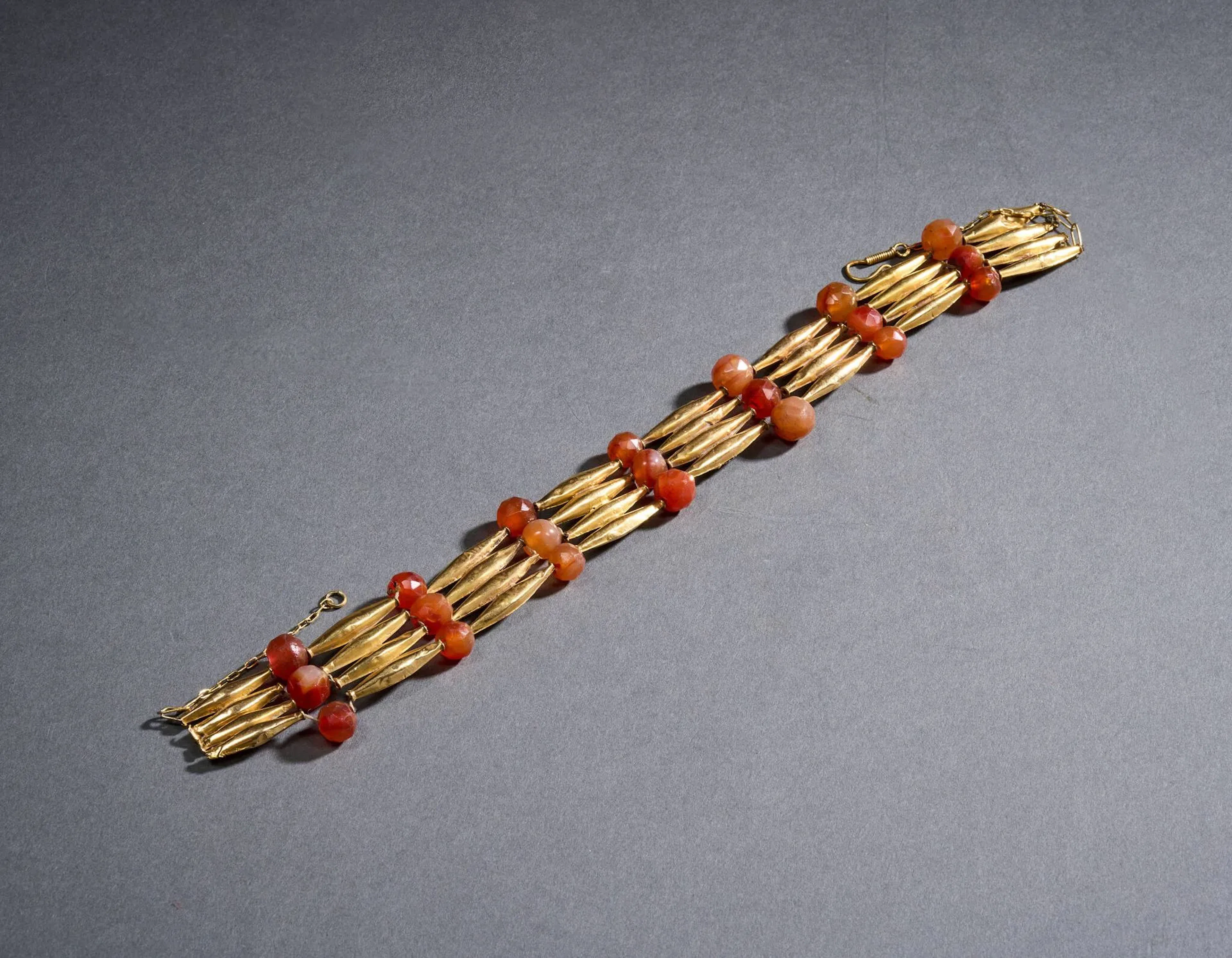 Collier draperie en or (585 millièmes) et cornaline, à décor alterné de perles en cornaline facettées sur trois rangés et de perles tubulaires en or de forme légèrement oblongue sur quatre rangs, se fermant par une chaîne fantaisie et un fermoir en or (585 millièmes), rapportés. Petits chocs de l’or. Travail égyptien du XIXe siècle, dans le goût antique. Porte un poinçon de contrôle égyptien. L. 43 cm. Poids brut : 48,8 g.