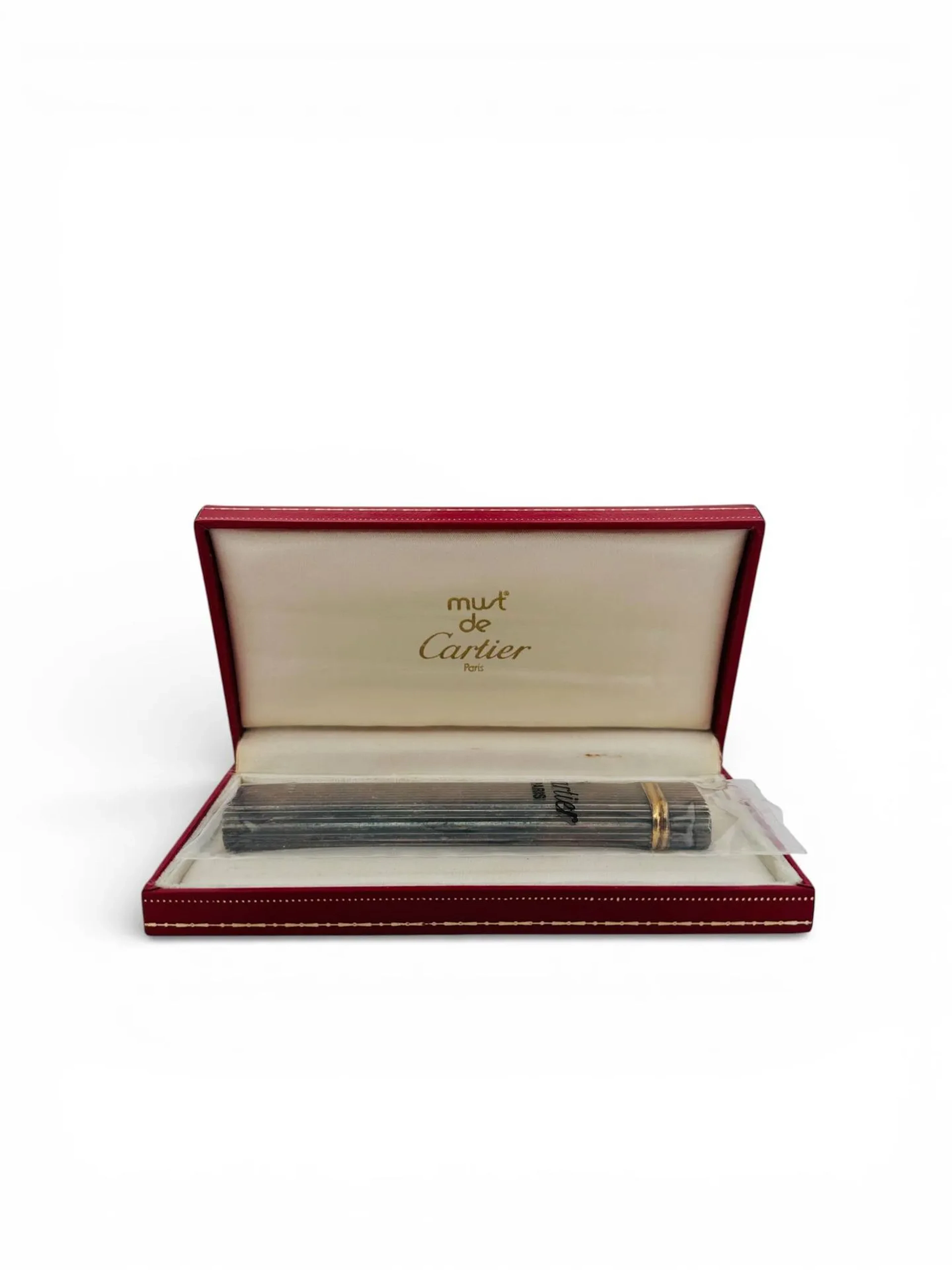 CARTIER Briquet de table en métal argenté, modèle à godrons, signé sous la base Cartier Paris, numéroté 02615X. Fonctionnel. Dans son écrin signé Must de Cartier et sa boîte. Odeur et trace d'humidité. Ht. 59 mm - Etat d'usage, petits chocs, à recharger en gaz.