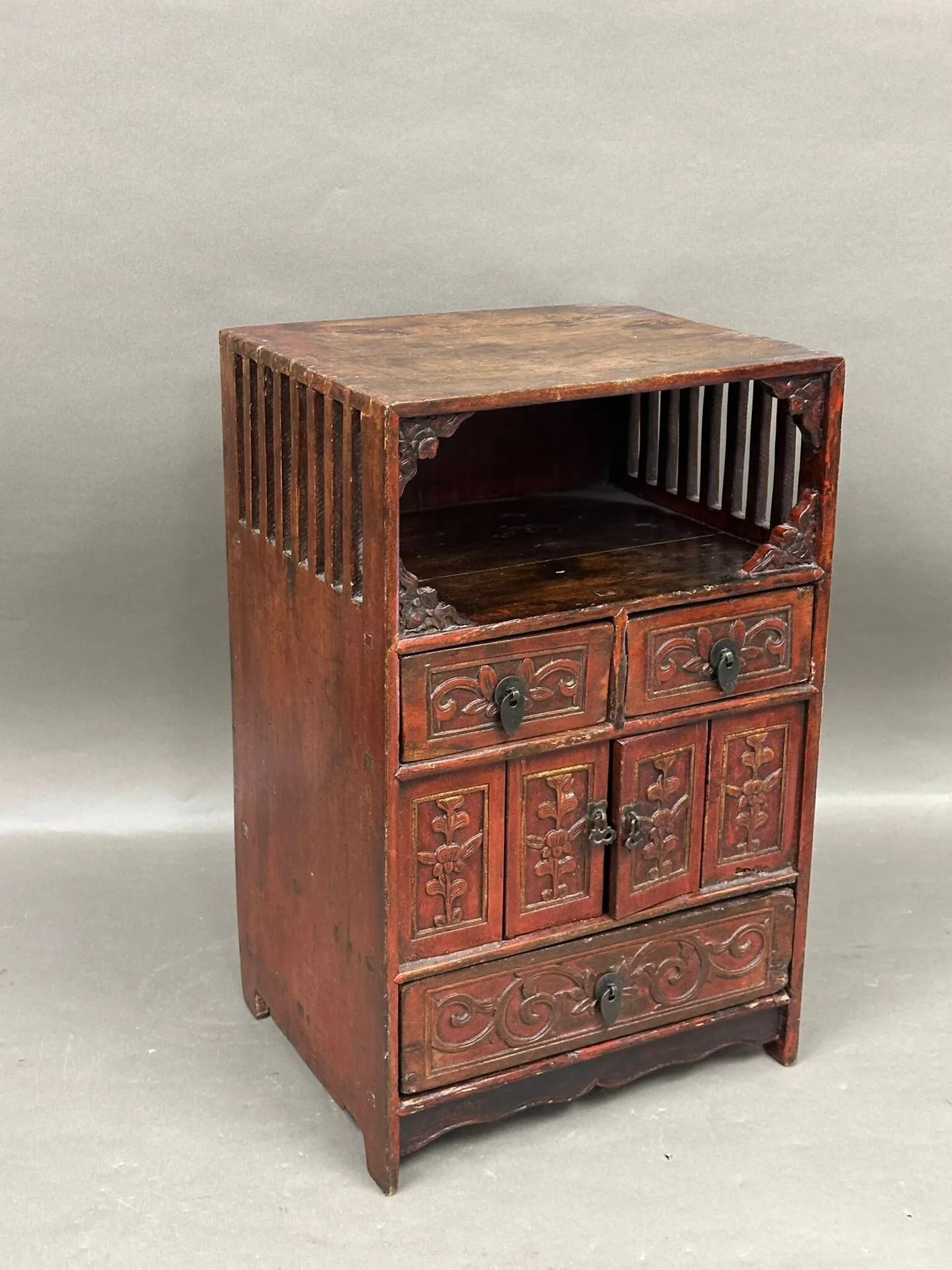 Petit meuble chinois quadripode en bois patiné rouge ouvrant en façade par une niche ajourée en haut, trois tiroirs et deux portes 48.5 x 30 x 25 cm