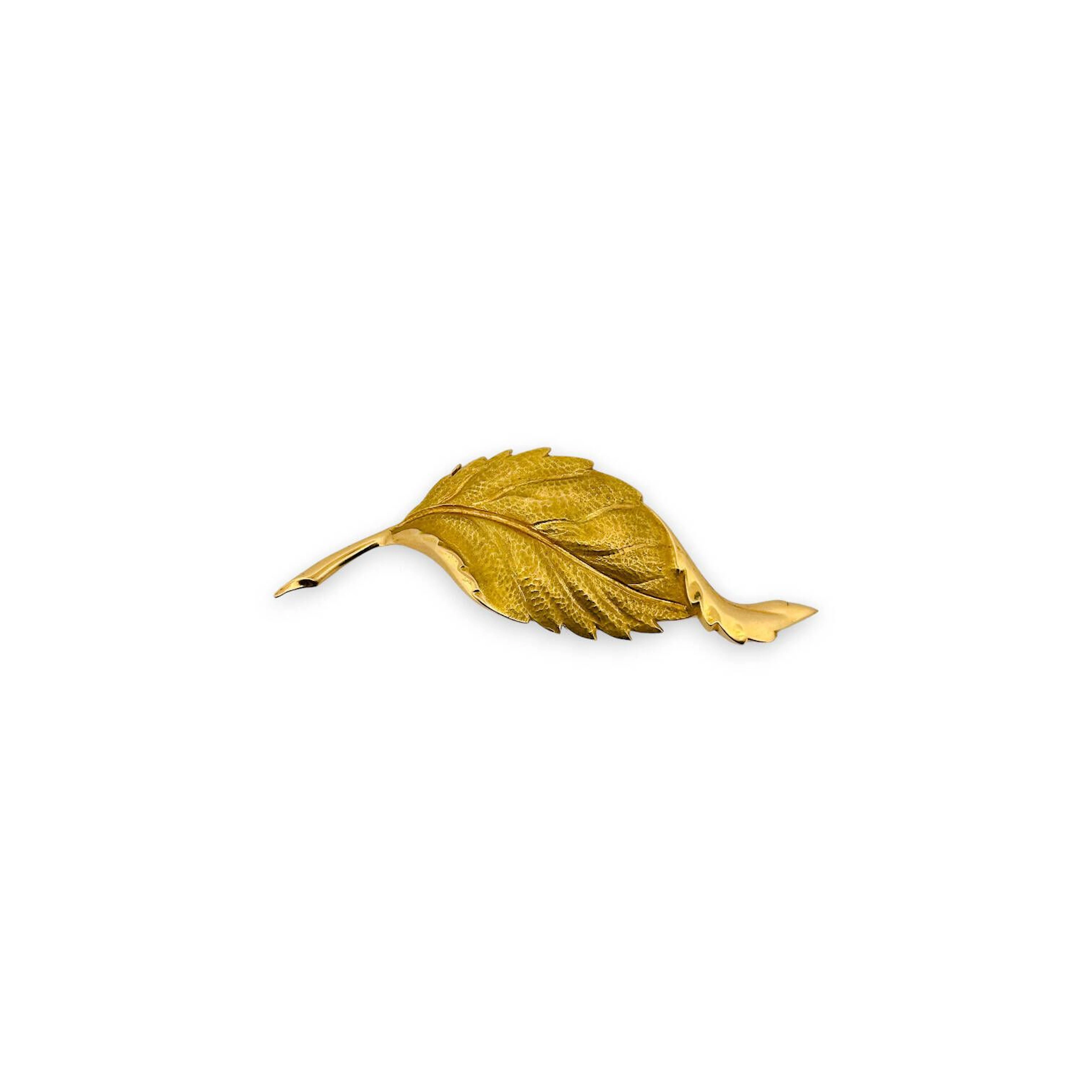 Broche en or jaune 18K (750), figurant une feuille nervurée, le décor traité en relief avec surface martelée et nervures ciselées, tige stylisée formant la queue. Épingle au revers avec fermoir à pompe. Longueur : 8 cm Poids brut : 12 g Poinçon : tête d’aigle.