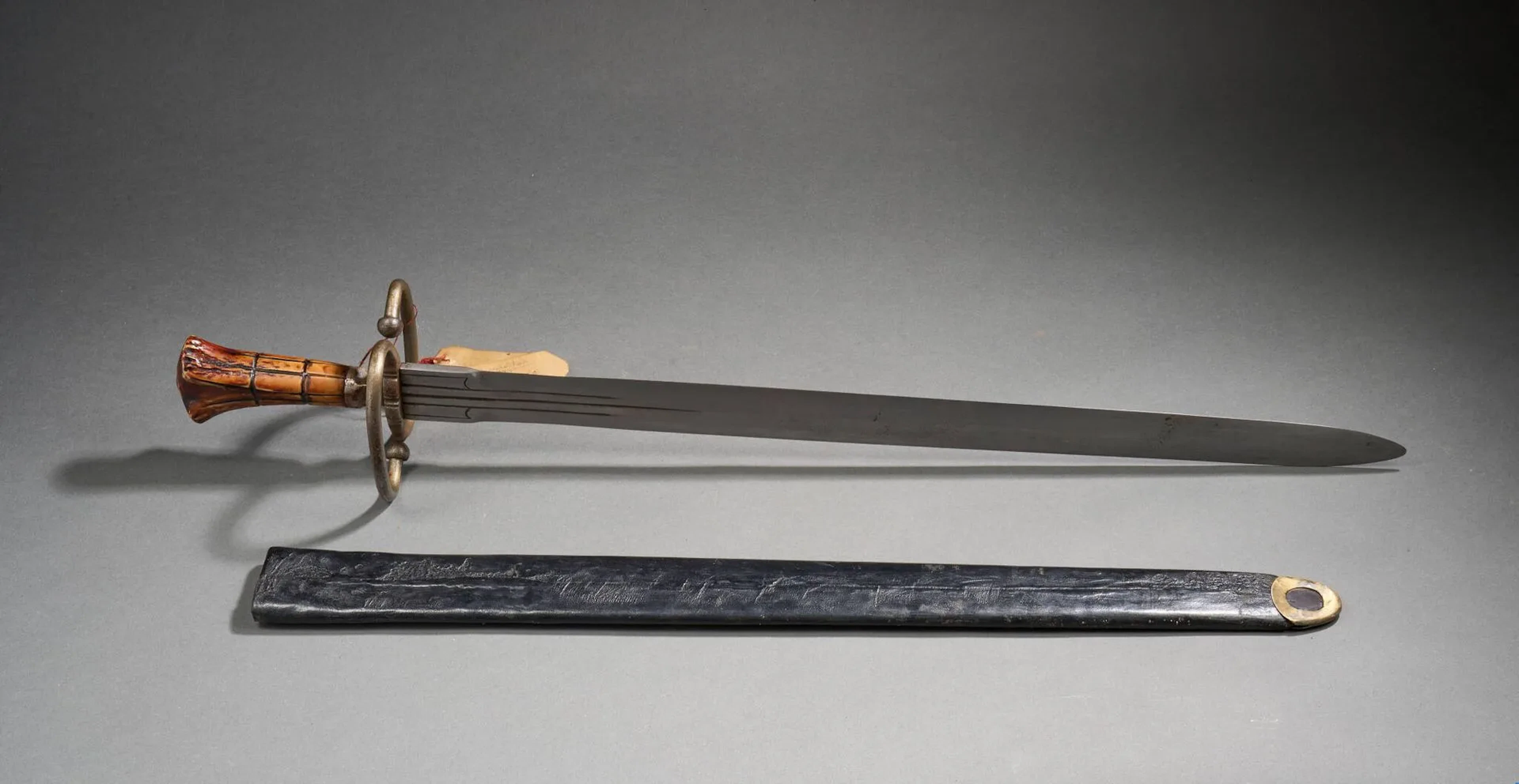 Épée germanique de Lansquenet dit Katzblager. Monture en bois de cervidé et fer. Fusée en bois de cerf sculpté et pièce de garde en S, caractéristique du modèle. Forte lame droite à trois gouttières au talon. Fourreau à âme en bois recouvert d’une basane et bouterolle laiton. Longueur totale : 82 cm. Travail de style milieu du XVIe siècle, probablement Violet le Duc (fourreau plus tardif).