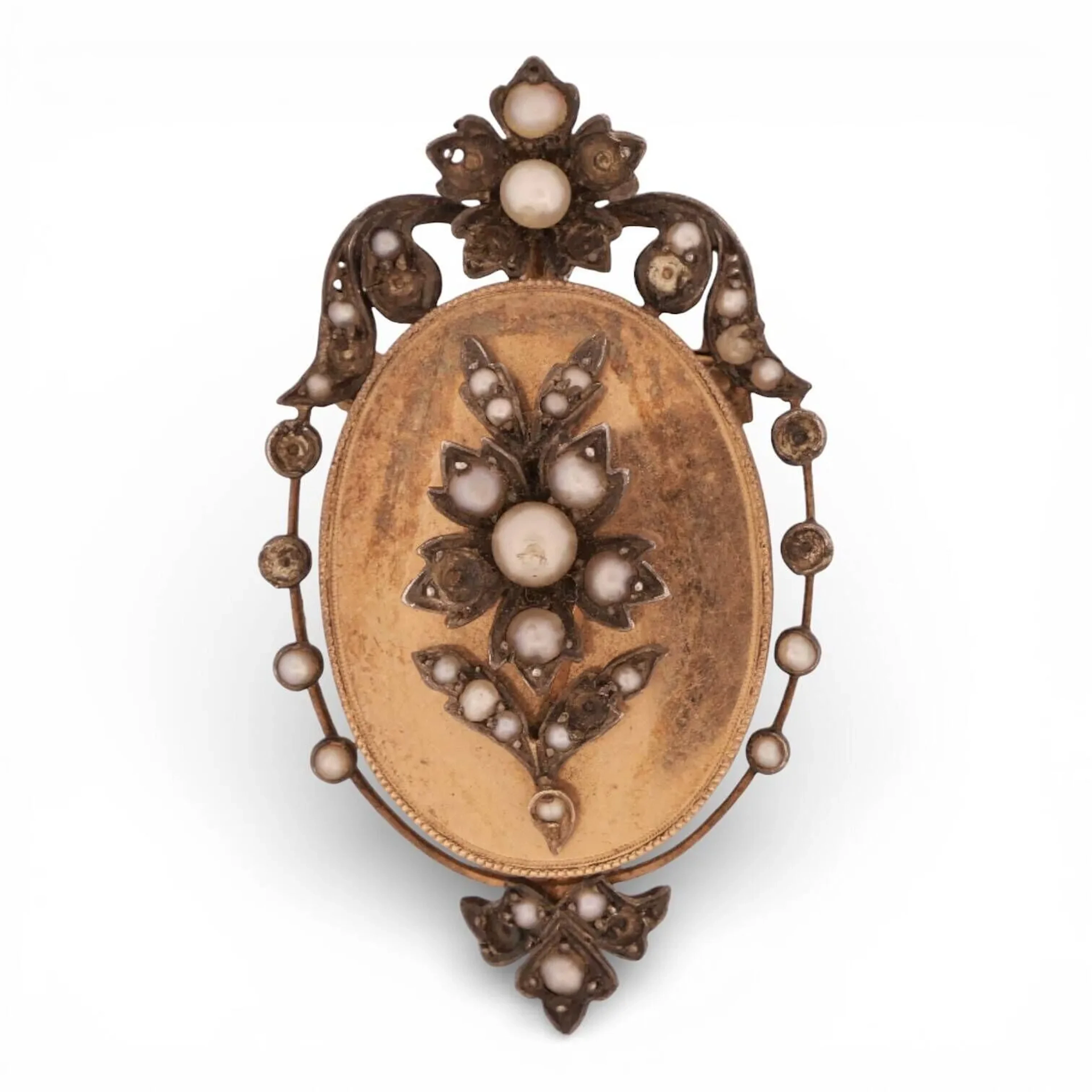 Broche-pendentif ovale en or 18K (750) et argent (800 minimum) appliqué d'un motif floral et feuillagé piqué de perles et entouré de motifs similaires. Dim. : 5 cm - Poids brut : 12.57 g. (manques)