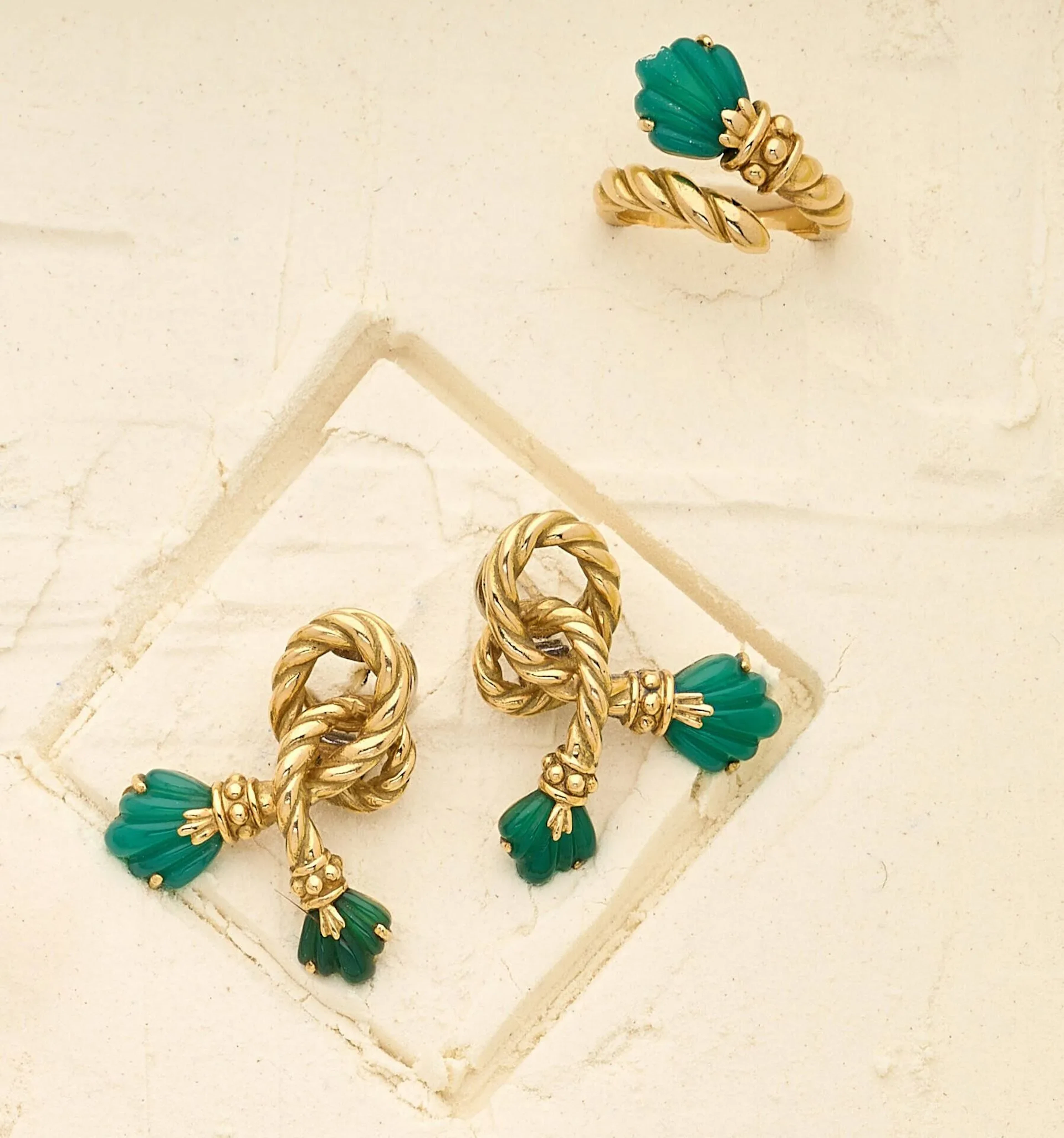 CHAUMET Demi-parure en or 18k (750e), comprenant une bague et une paire de clips d'oreilles, à décor de noeuds torsadés terminés de calcédoines vertes sculptées en palmettes. (un manque de matière à la bague) Signée Chaumet Paris, avec poinçon de maître. Vers 1970. Poids brut : 26.70 g. Hauteurs : 3 cm. Tour de doigt : 55.