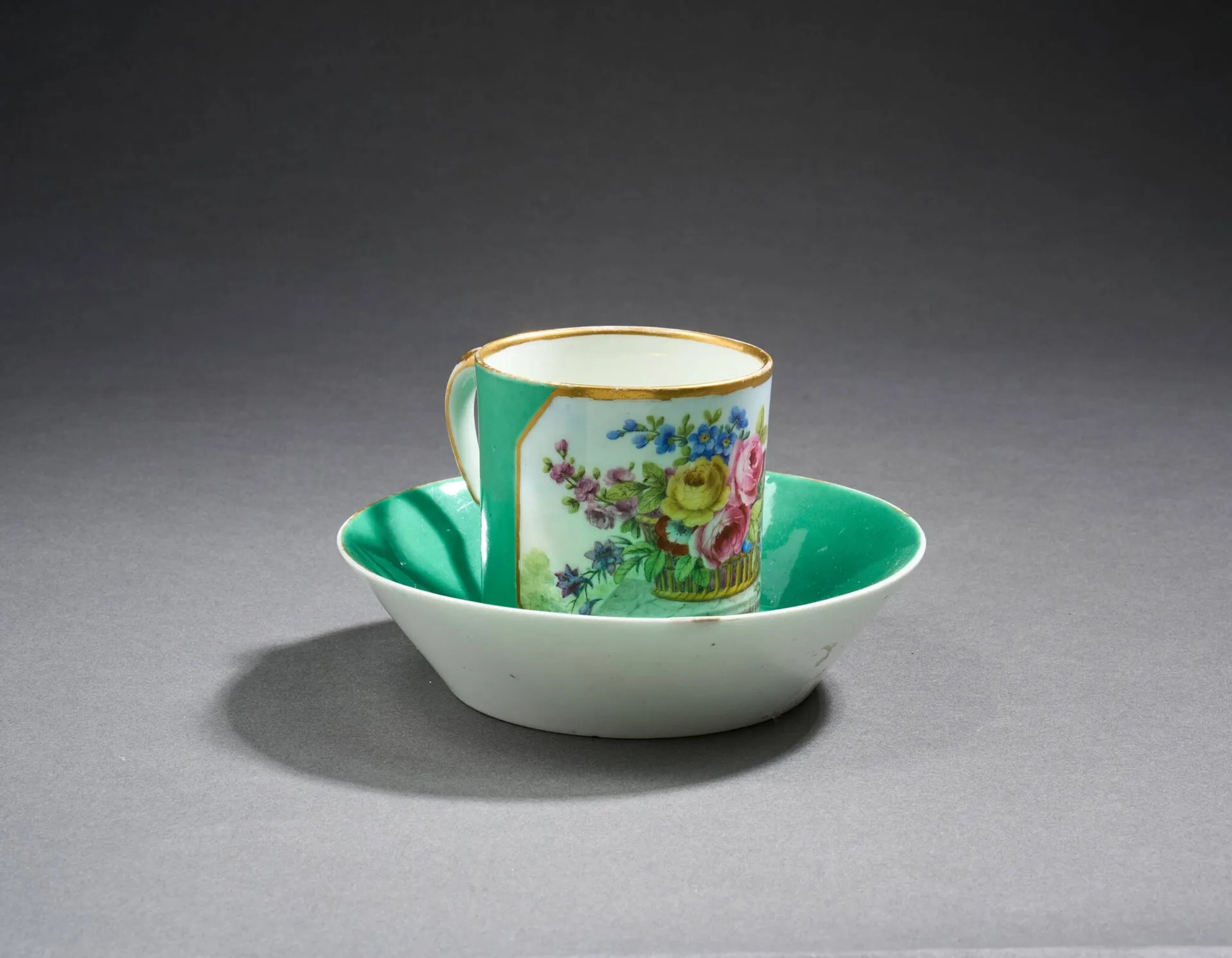 SÈVRES Tasse litron et sa soucoupe en porcelaine à fond vert et décor d’un cartouche rectangulaire à angles coupés centré d’un bouquet de fleurs polychrome, filets or sur les bords. Usures de l’or, petite restauration en bordure de la soucoupe. Manufacture nationale de Sèvres, époque révolutionnaire. Marque en bleu sous couverte « Sèvres » et marque du peintre de fleurs Jean Baptiste Tandard l'Aîné (actif 1754-1800). H. 6,8 x D. 13,5 cm.