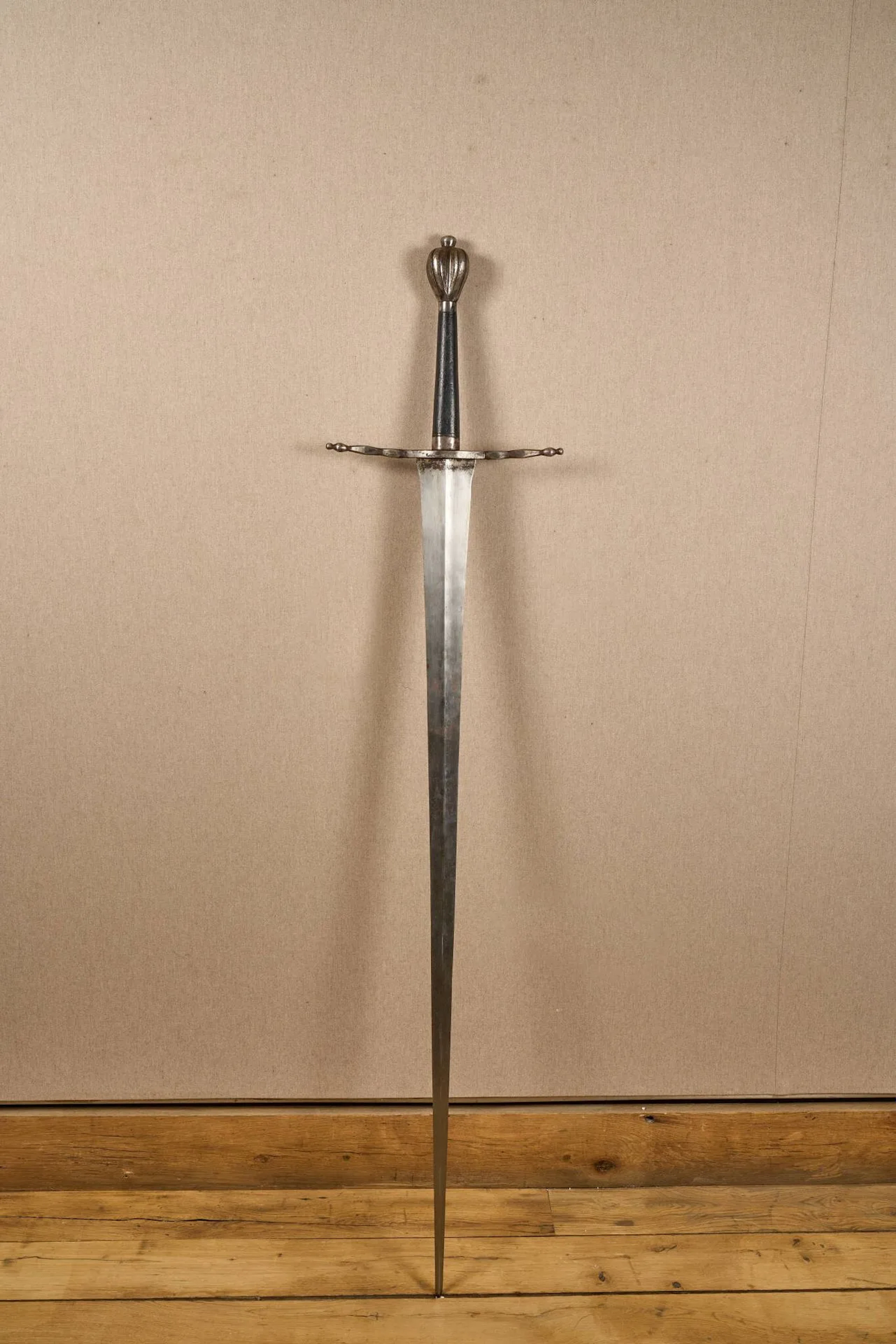 Forte épée à deux mains. Pommeau piriforme, pièce de garde à deux quillons droits. Fusée en bois noirci. Forte lame à double tranchant, arrête médiane et estoc aigu. Longueur totale : 166 cm. Travail de style, probablement Viollet le Duc.