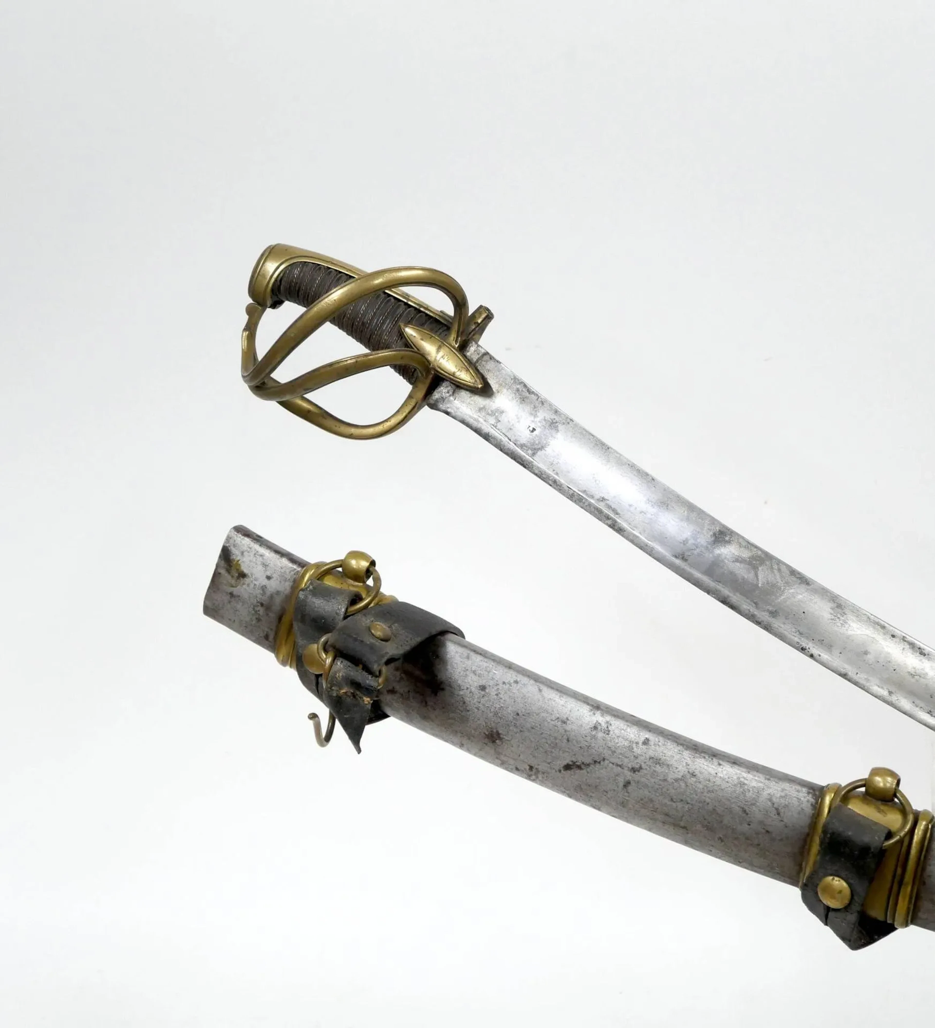 Fort sabre d’officier de cavalerie légère au modèle an XI. Monture en laiton garde à la chasseur à deux branches de garde reliant l’arc de jointure. Branches décorées au trait, croisière en amande (manque la pointe à l’une). Quillon coupé. Calotte ovale à longue queue, fusée en bois recouverte de cuir filigrané. Lame de prise anglaise (restes de marquage « GUNBY » au talon, forte courbure, à pans creux et contre-tranchant en langue de carpe. Fourreau en acier à deux larges bracelets laiton (manque la cuvette). L. totale : 95 cm. France, époque 1er Empire. Complet de ses deux suspentes en cuir et attaches laiton.
