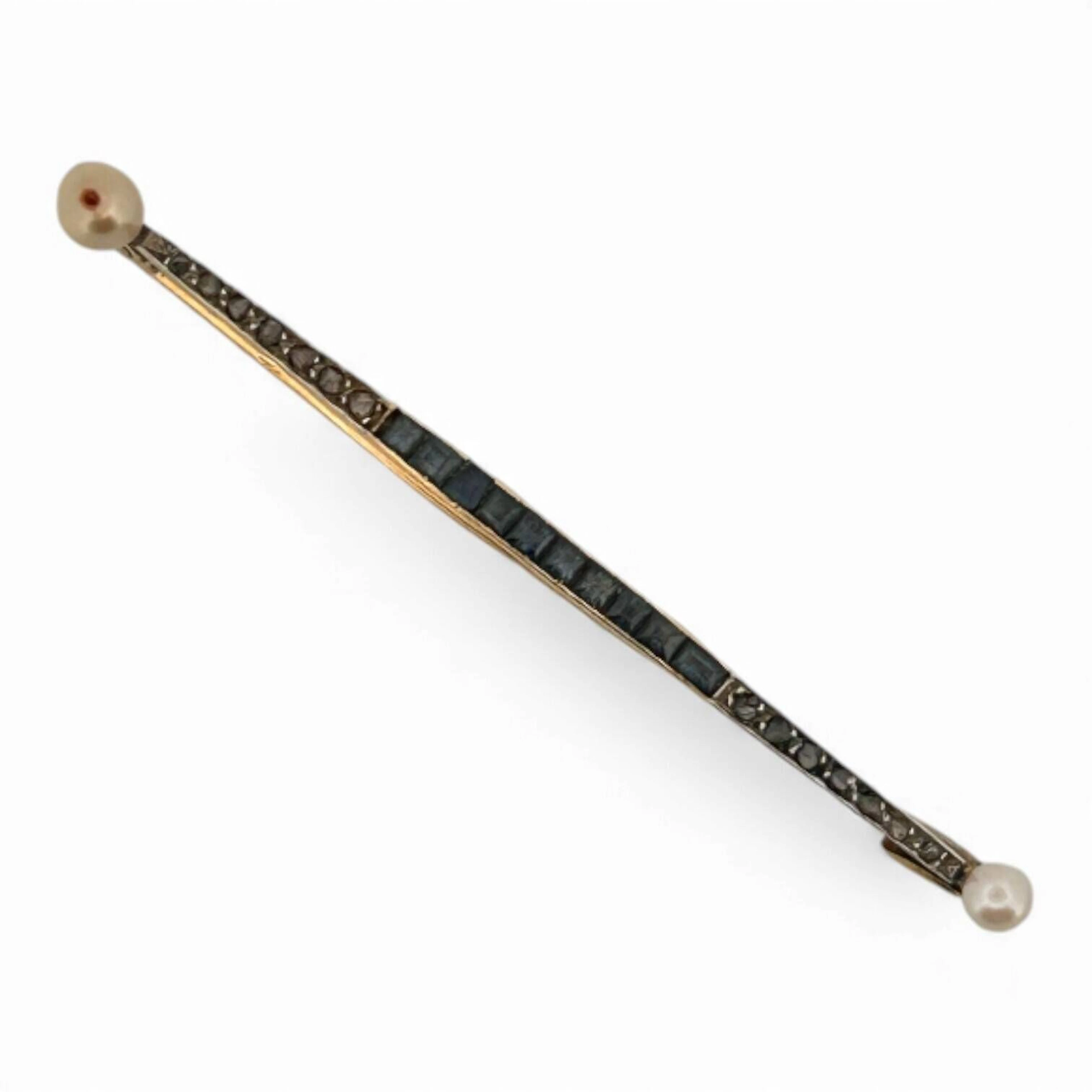 Broche ligne en or jaune 18K (750) sertie d'une ligne de saphirs calibrés et diamants taillés en roses, les extrémités serties d'une perle de culture ronde ou baroque. Poids brut : 2.83 g. (chocs ayant entrainés un manque de matière)