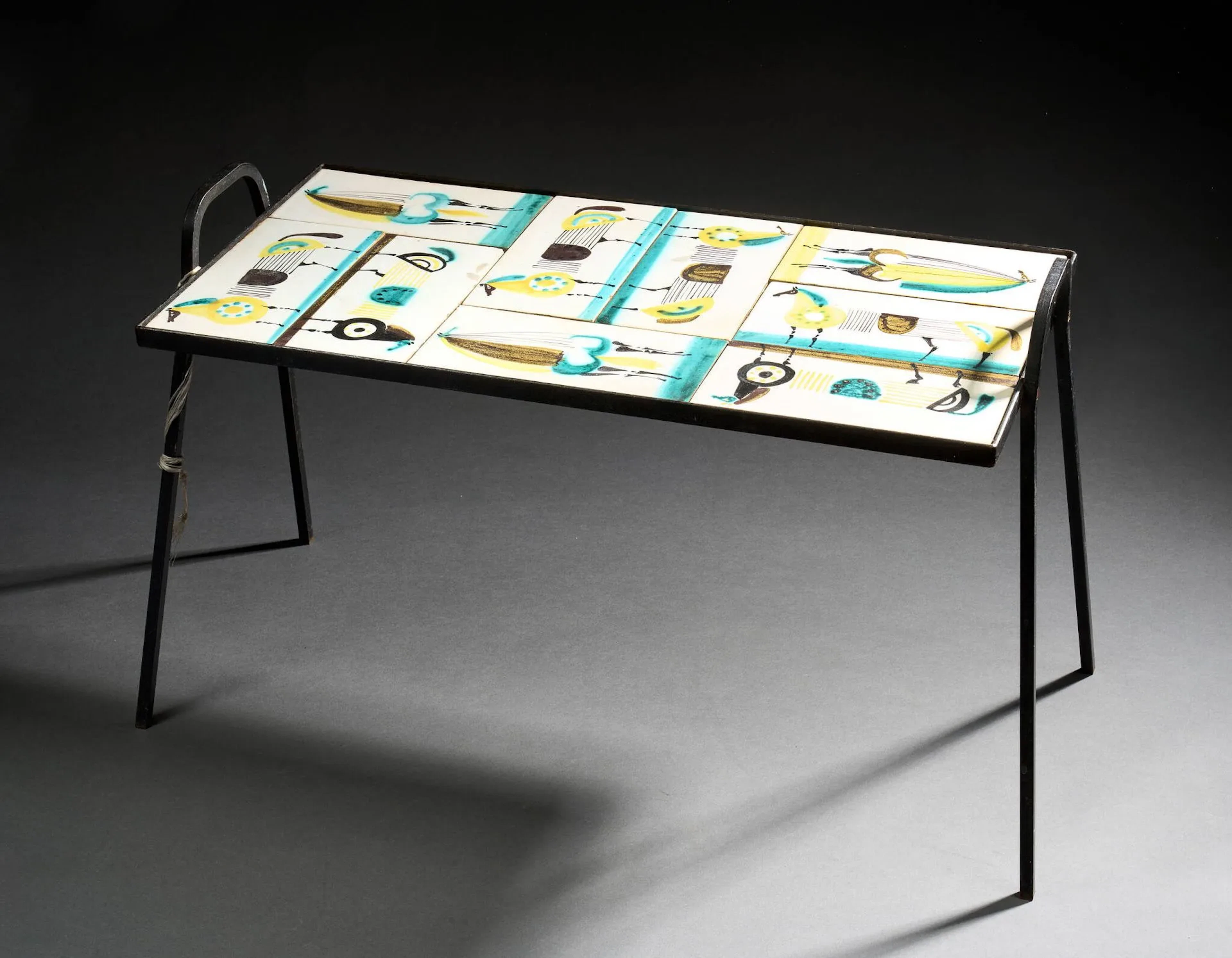 Roger CAPRON (1922-2006) Table basse, circa 1955, à plateau rectangulaire aménagé de carreaux de céramiques polychromes à décor de chevaux stylisés disposé sur une structure en métal laqué noir et reposant sur un double piètement en U. Non signée H. : 41.5 cm. - L. : 64 cm. - P. : 31.5 cm. (Usures, rayures) Note : - Nous remercions Phillipe Capron pour les renseignements fournis