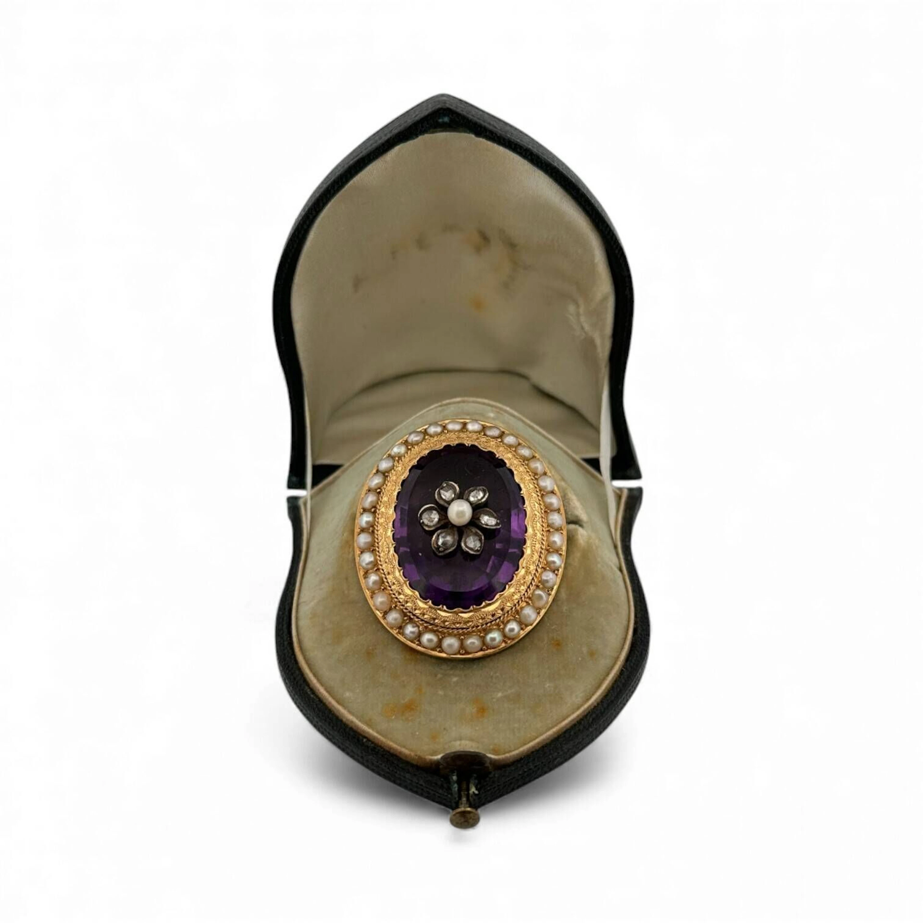 Broche ovale en or jaune 18K (750) sertie d'une importante améthyste appliquée d'un fleur formée diamants taillés en roses dans un entourage de perles boutons irrégulières. Conservée dans un écrin. Poids brut : 19.1 g.