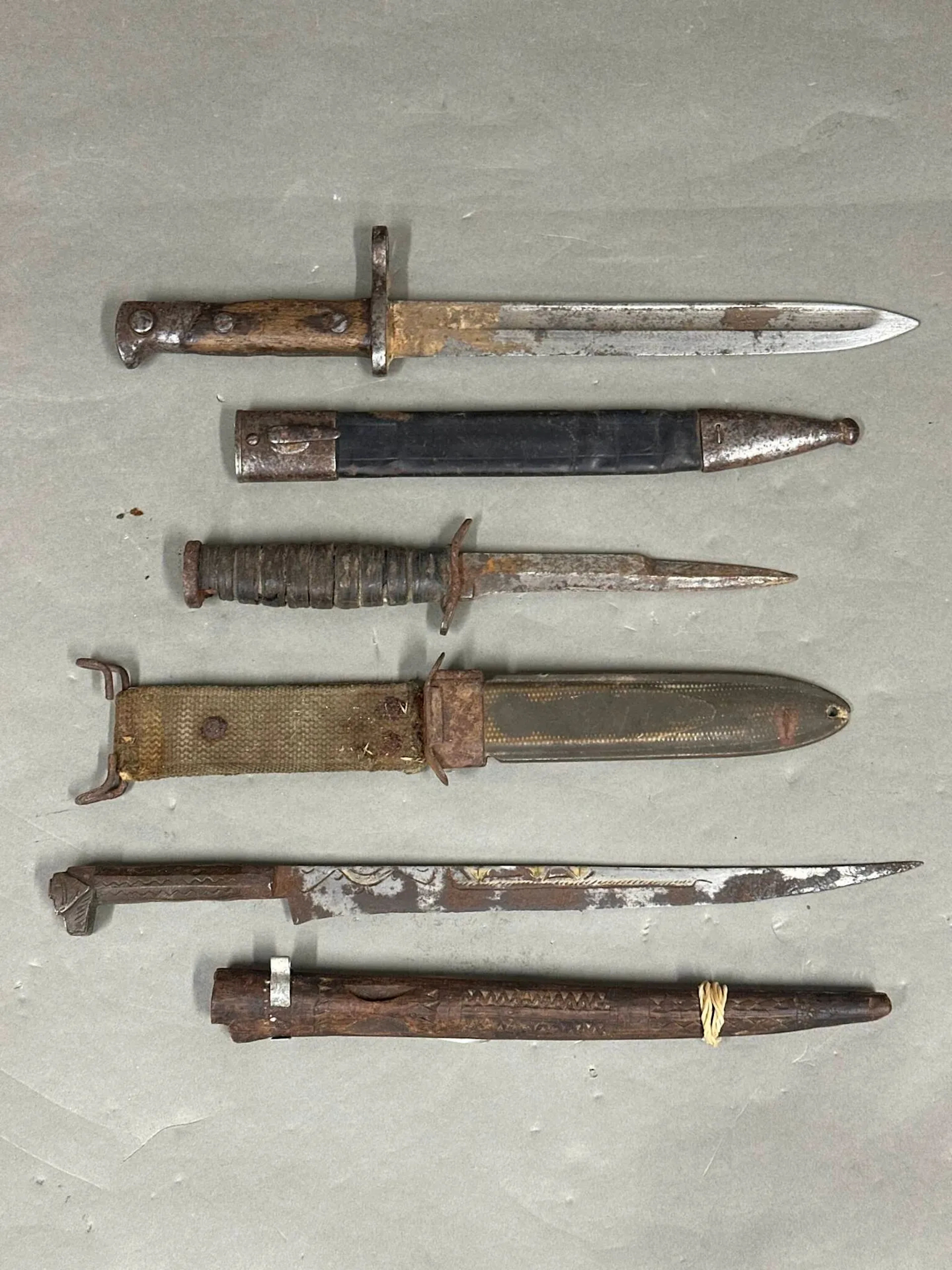Lot comprenant Une baïonnette type Mauser avec fourreau cuir et deux garnitures en fer dans son état de découverte. Un poignard type USM3 fabrication civile. Lame réduite par affutage. Fourreau type USM8. En l'état Un poignard flissah. Monture en fer et lame incrustée de laiton. Fourreau en bois en deux parties (accidents) Algérie, première moitié du XXe siècle
