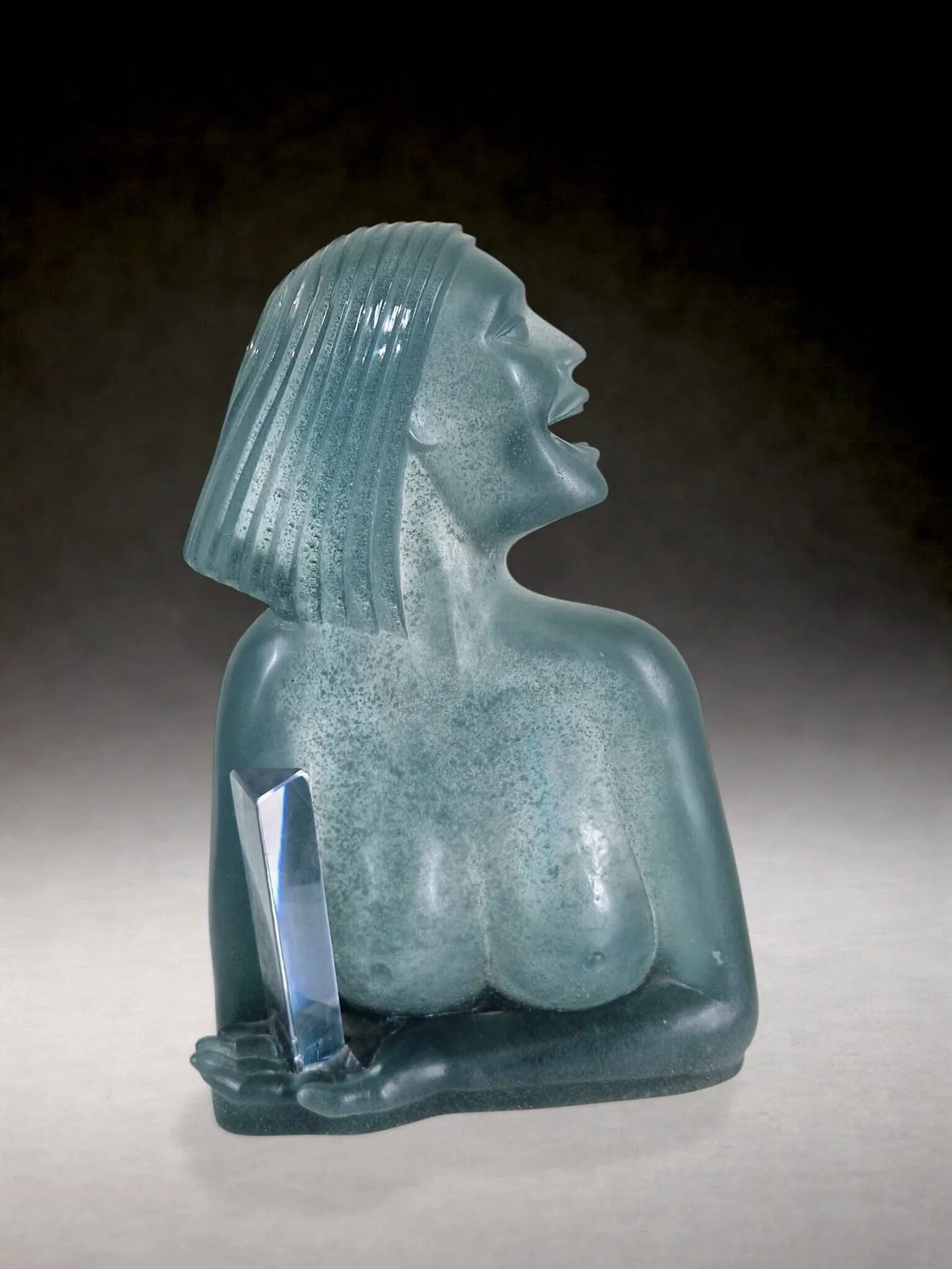 Dan DAYLEY (Etats-Unis, né en 1947) pour DAUM « La Dame », sculpture en pâte de verre dans les tons gris-vert et bloc de cristal. Signature de l’artiste sur le côté et cachet de la cristallerie au dos. éclats en bas du bloc de cristal dans la main du personnage H. 48 cm x L. 32 cm x P. 16 cm
