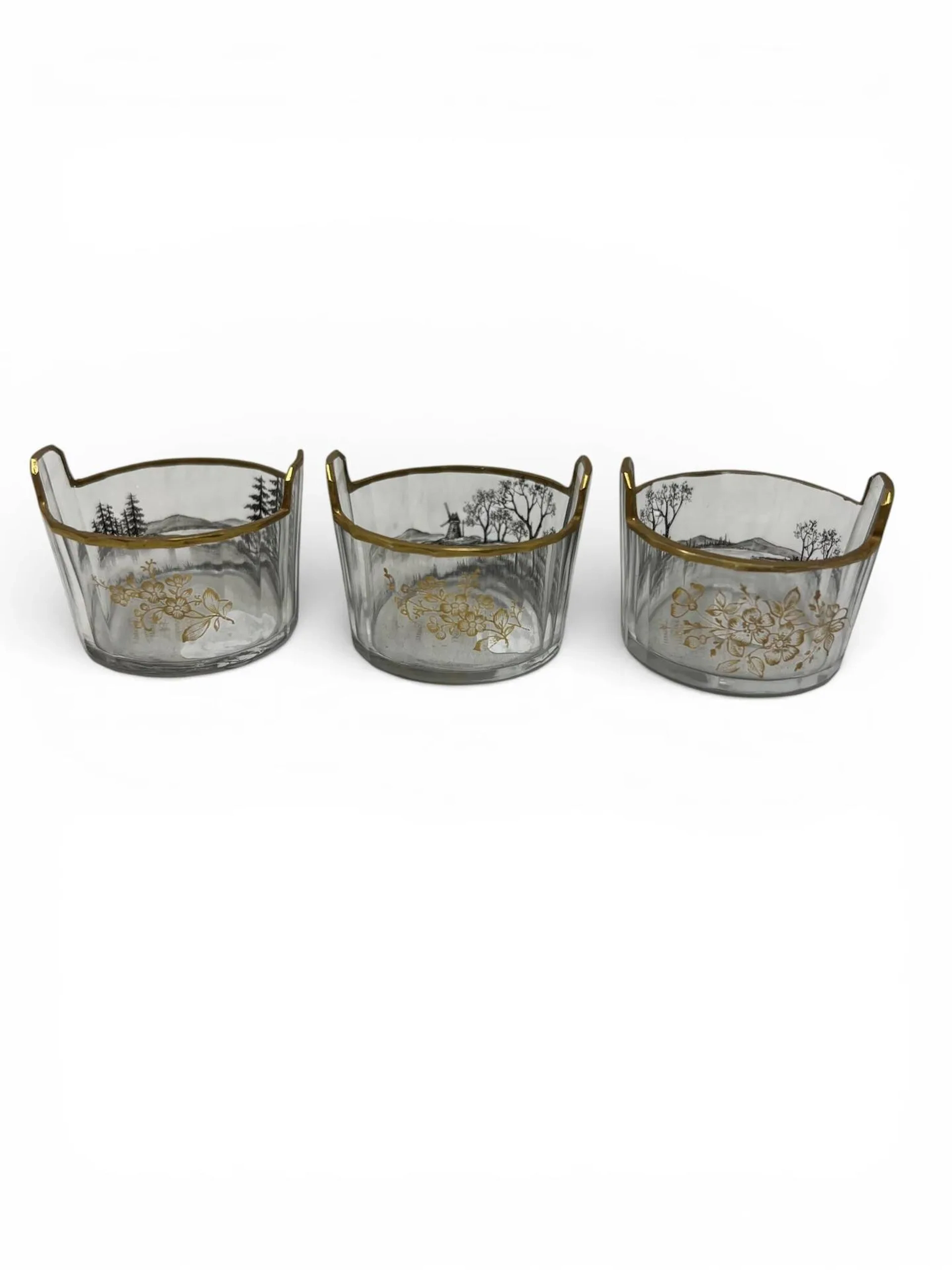 DAUM – NANCY Lots de trois salerons en verre blanc à corps circulaire et deux anses pleines latérales. Décor en grisaille de paysages lacustres et de fleurs rehaussé de dorure (infimes égrenures). Signés et situés à l’or au revers. Haut. 3,5 cm – Diam. 4,5 cm Bibliographie : Noël Daum, Daum, maîtres verriers, Édita-Denoël, Lausanne, 1980, saleron à la forme similaire à nos modèles reproduit p. 120.