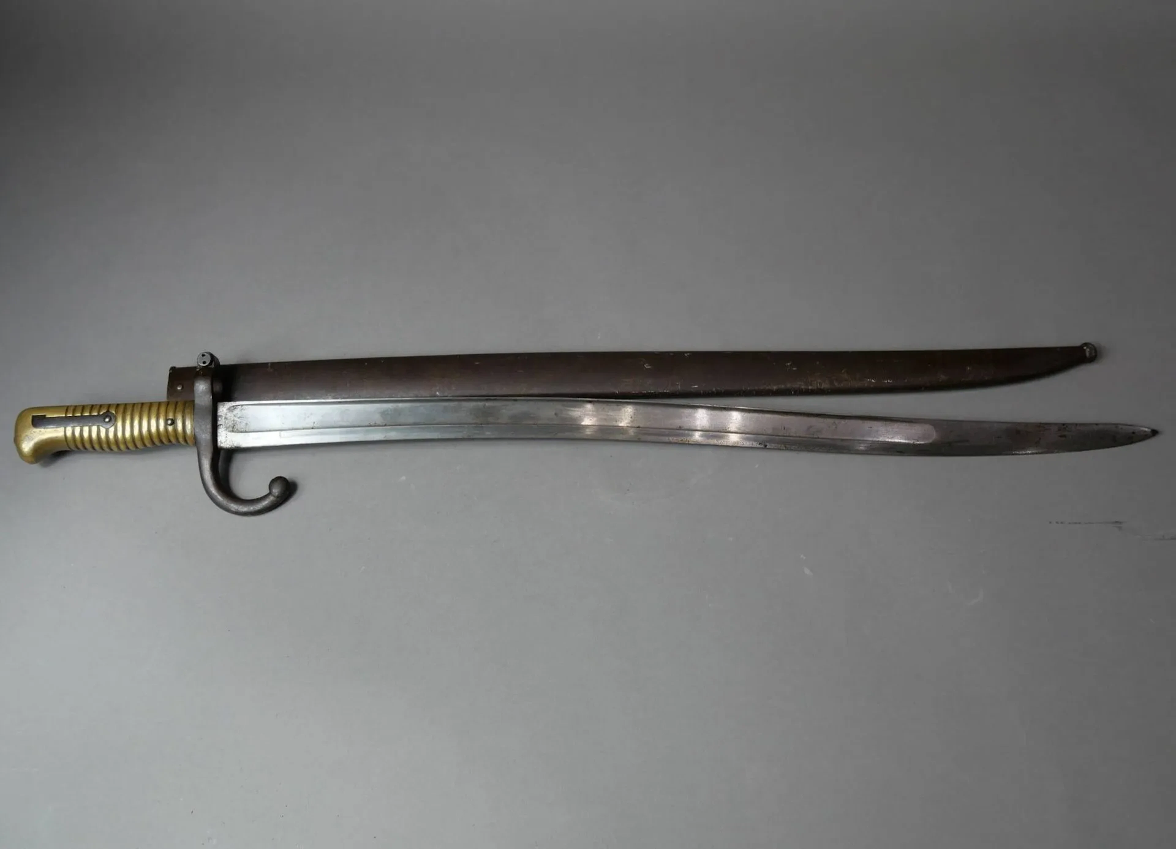 Baïonnette modèle 1866 pour fusil Chassepot. Monture en laiton et quillon fer. Lame à la yatagan de la manufacture Impériale de Chatellerault, date 1868. Fourreau en acier au même numéro. Longueur totale : 69 cm. France, Époque Second Empire.