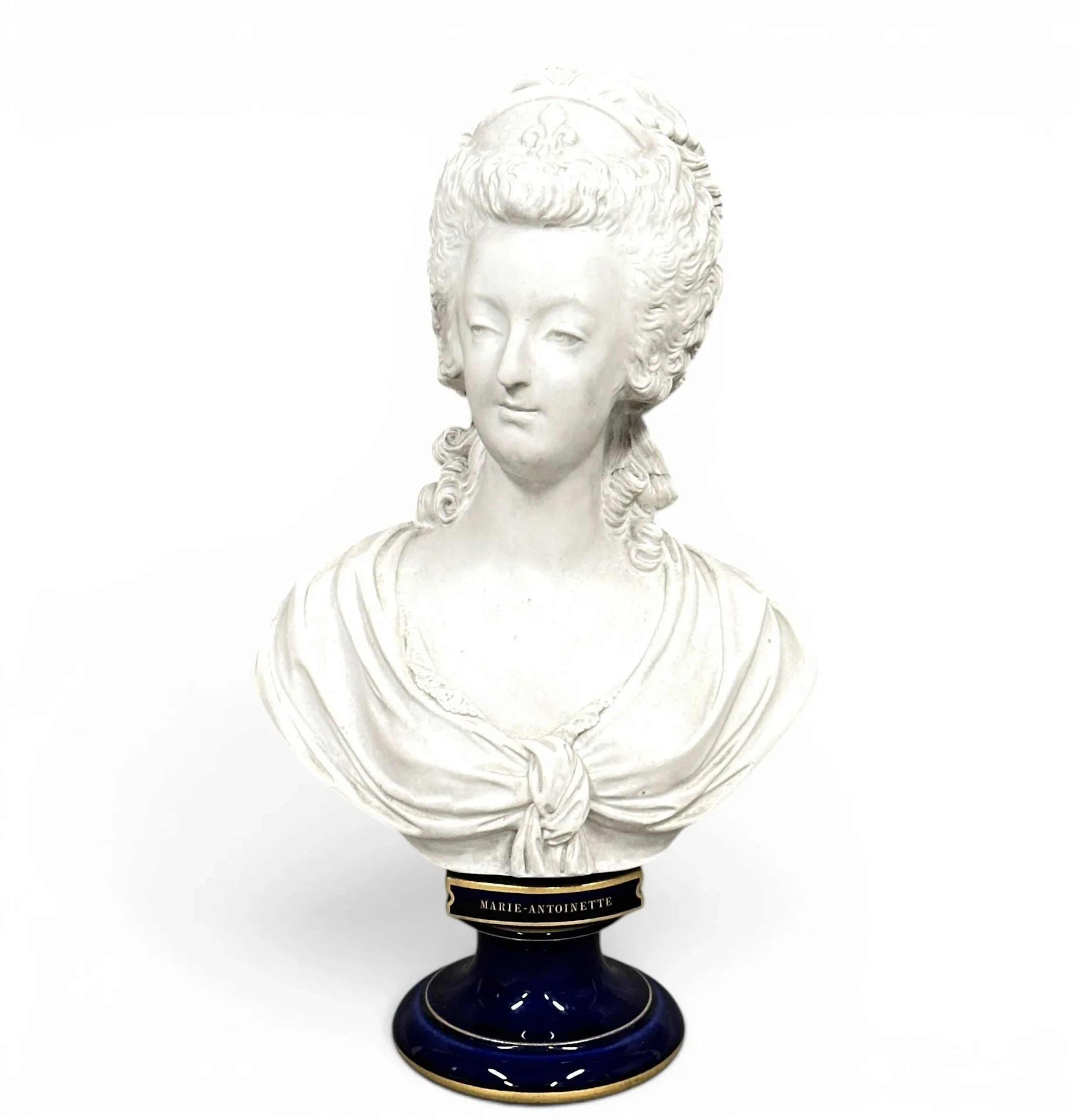 Louis-Simon BOIZOT (1743-1809), d’après. Buste de Marie-Antoinette, reine de France, coiffée d’un diadème fleurdelisé. Biscuit de porcelaine dure, reposant sur un piédouche circulaire en porcelaine à fond beau bleu et filet or sur les bords. Manufacture nationale de Sèvres, 1876. Marque au revers au tampon vert de fabrication «S. 71», marque au tampon rouge de décor au RF entrelacé «doré à Sèvres» datée (18)76 ; marque des biscuits au tampon en creux «Sèvres» et de répareur au dos. Portant une ancienne étiquette de l’enseigne «Aux Arts Céramiques» tenue par L. Boutigny, au Palais-Royal à Paris. H. 31 cm.