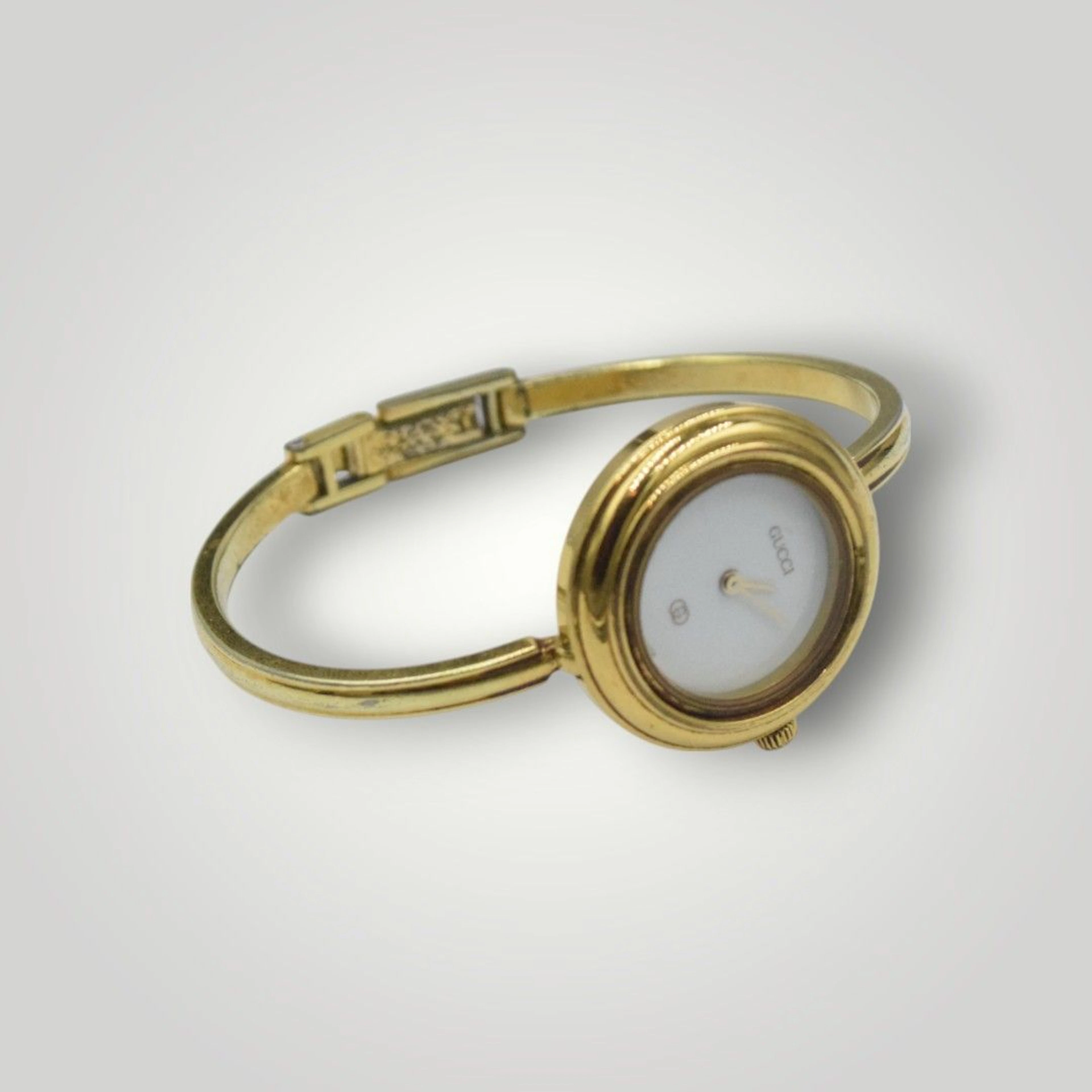 GUCCI Montre de dame à bracelet rigide en métal doré, cadran blanc siglé, fermoir siglé. Oxydations, cadran rayé