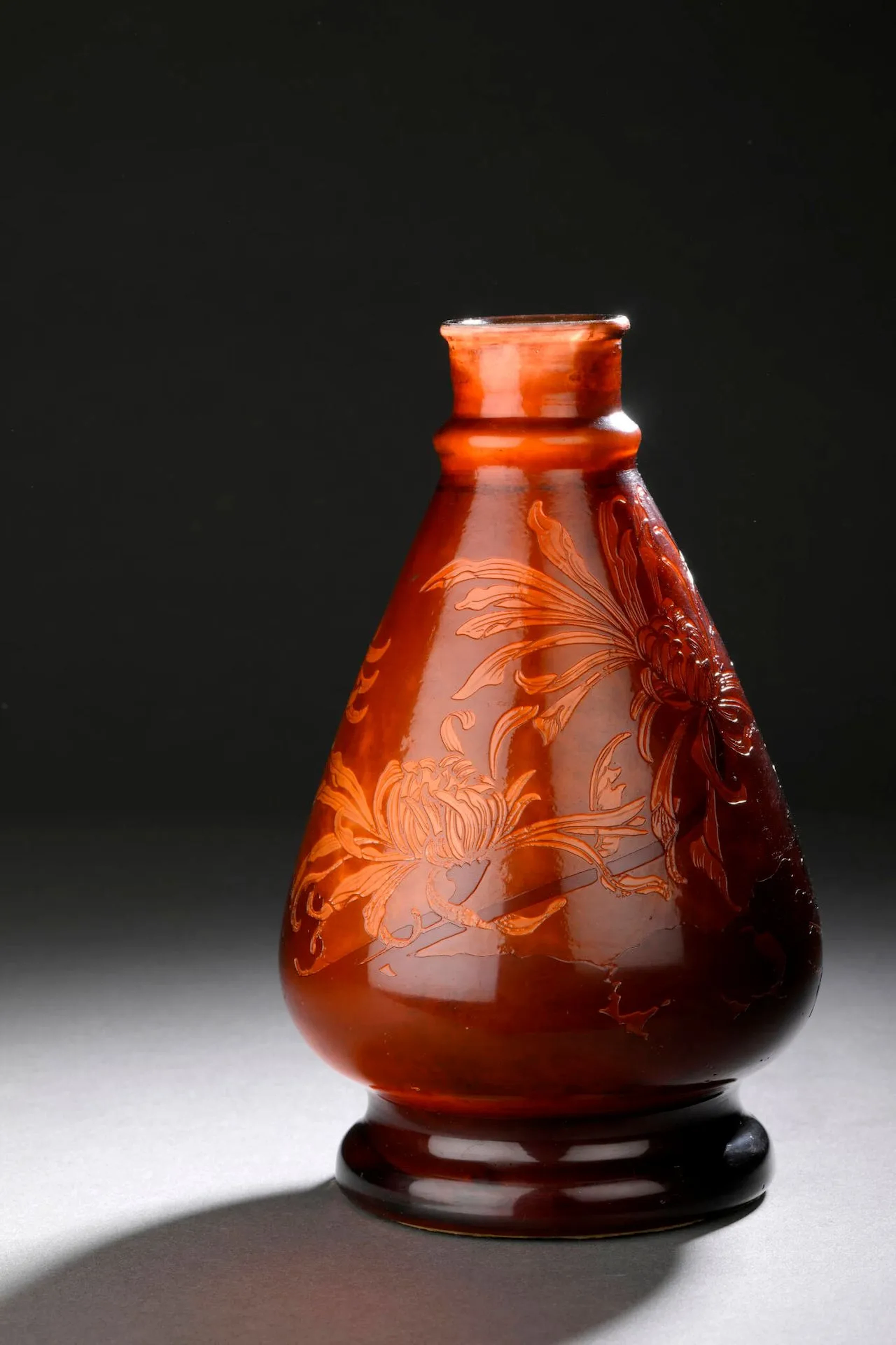 Émile GALLÉ (1846 – 1904) Vase toupie à partie supérieure baguée et col ourlé sur piédouche circulaire. Épreuve en verre brun rouge sur fond rouge. Décor de chrysanthèmes gravé en camée à l’acide sur fond moiré façon pierre dure. Signé dans le décor. Haut. 21 cm