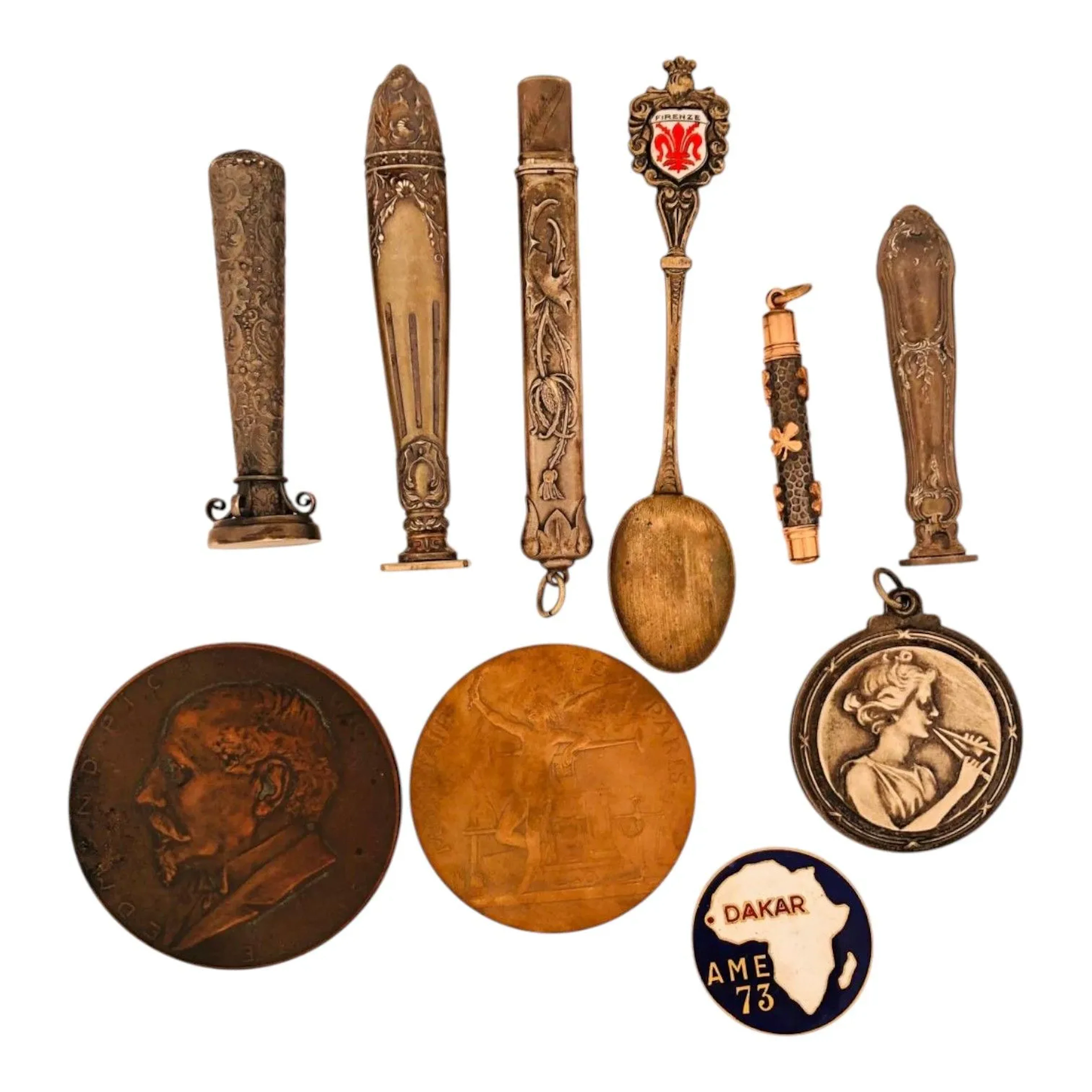 Réunion d'objets de vitrine : - un sceau en argent fourré la prise rocaille, la matrice ovale aveugle. Poinçon Minerve. Dans son écrin. Poids brut : 9 g. - un sceau en argent fourré la prise de style Louis XVI, la matrice rectangle aveugle. Poinçon Minerve. Poids brut : 15.20 g. - un sceau en métal argent la prise à décor d'enroulements et de fleurs, la matrice ovale aveugle. - un porte crayon en argent à décor de houx. Poinçon tête de sanglier. L. : 8.20 cm - Poids : 5.80 g. - un pendentif secret d'époque Art Nouveau découvrant un miroir. Diam. : 4 cm. - une médaille en bronze de la monnaie de Paris pour l'Exposition Universelle 1900 - une médaille en bronze. Avers : Edmond Picard. Revers : un hérisson "je gène". - un porte-mine en métal à décor de trèfle à quatre feuilles - une cuiller Firenze en argent (800). Poids brut : 9.40 g - une broche Arthus Bertrand en émaux cloisonnés AME 73 - Dakar