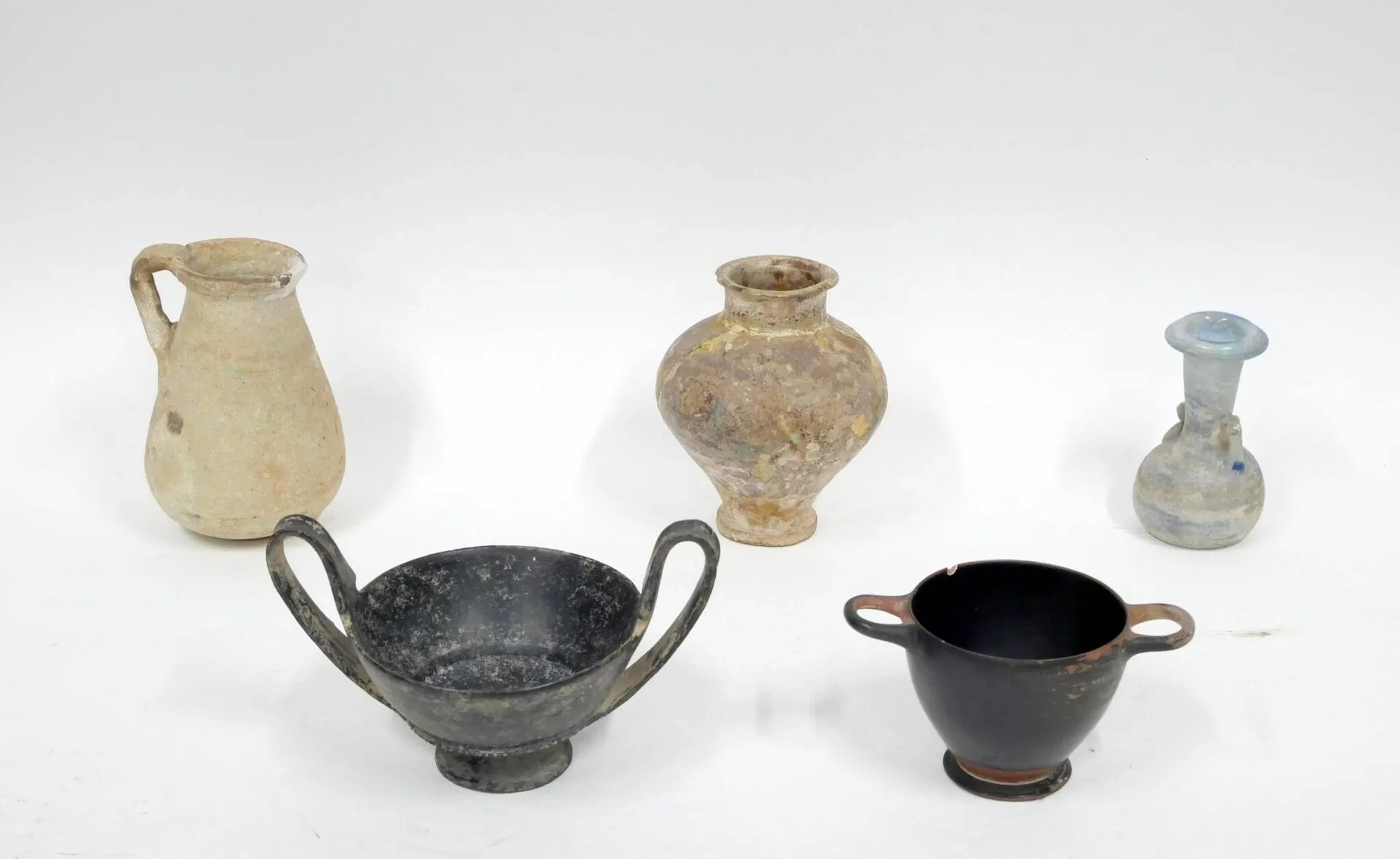 Lot composé d’un skyphos, d’un canthare, d’un pichet à anse et d’un vase à panse globulaire. On y joint un verre de style antique. Arts grec, étrusque, romain et période islamique, du VIe siècle av. J.-C. au IXe siècle apr. J.-C. Céramiques diverses : bucchero, vernis noir, terre cuite et argile glaçurée. H : 13 cm env. (le plus grand)