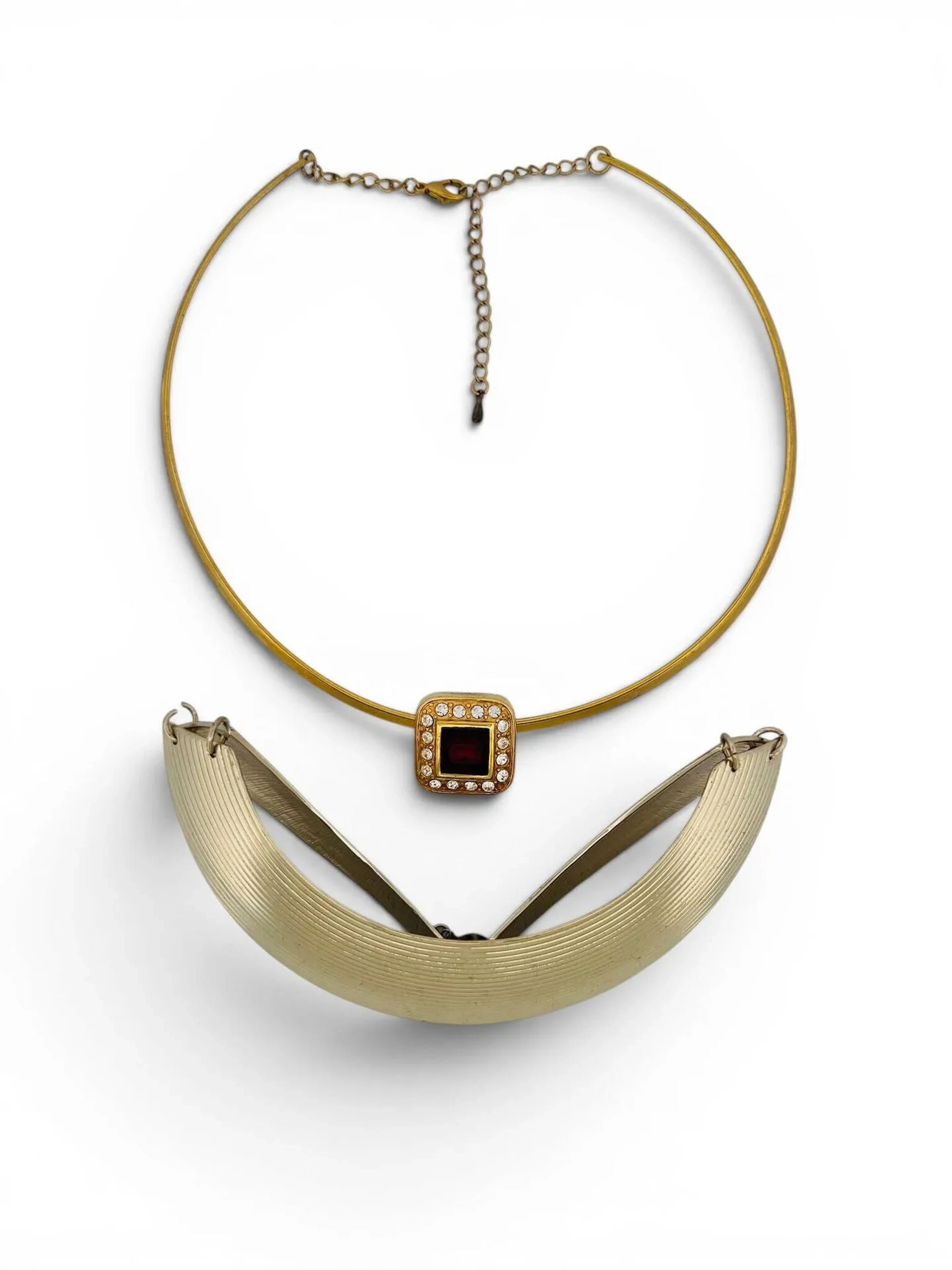Ensemble de deux colliers fantaisies comprenant: - Collier torque articulé en métal doré. - Collier ras de cou agrémenté d'un pendentif centré d'une pierre de synthèse rouge dans un tourage de strass. En l'état