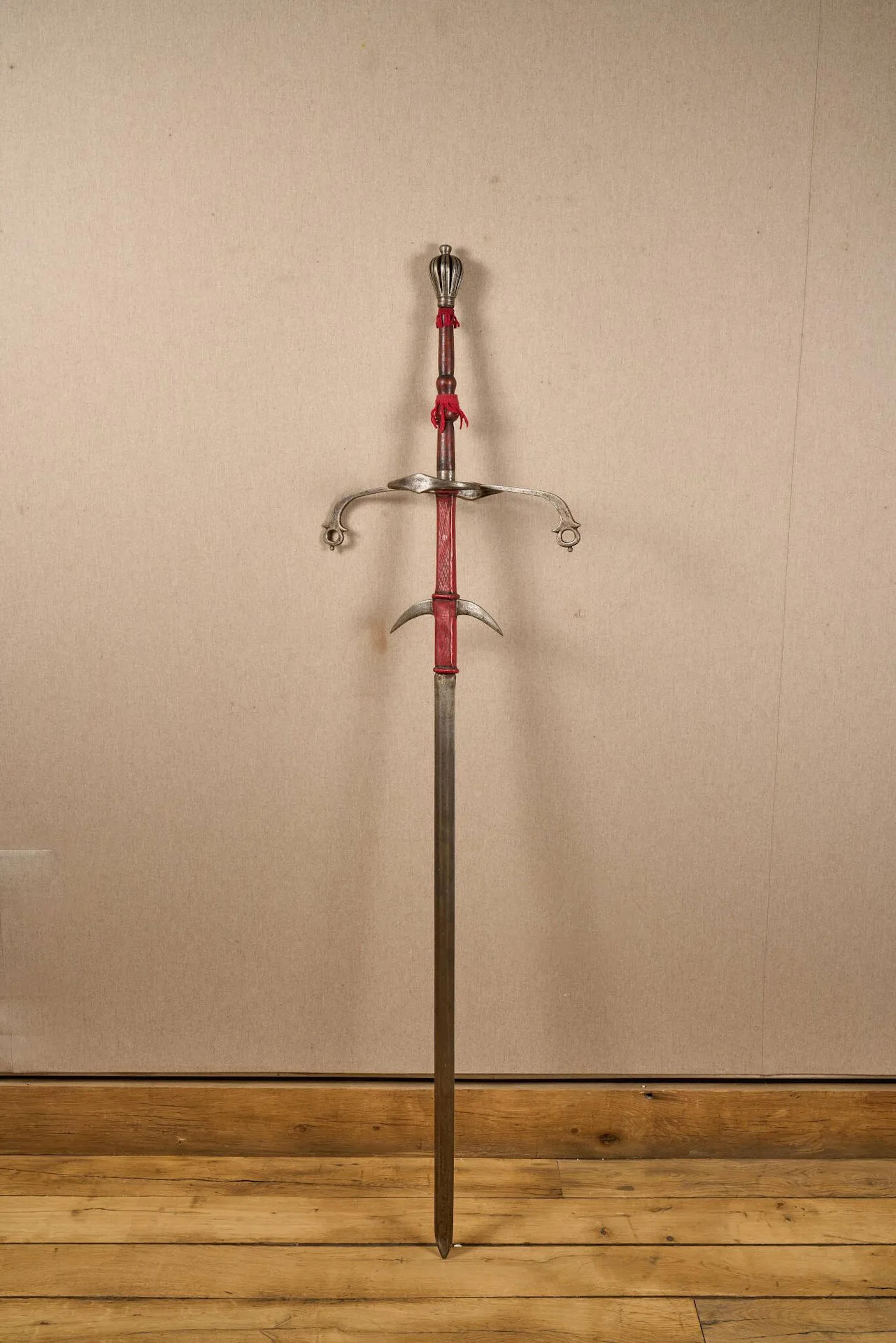Épée germanique à deux mains dit zweihander. Monture en fer. Pommeau piriforme, pièce de garde à deux anneaux et quillons courbes. Fusée en bois tourné. Forte lame à ricasso couvert d’un cuir, deux puissants ergots puis à méplat et double tranchant. Longueur totale : 176 cm. Travail de style 1580, probablement Viollet le Duc (exception du bois et cuir).